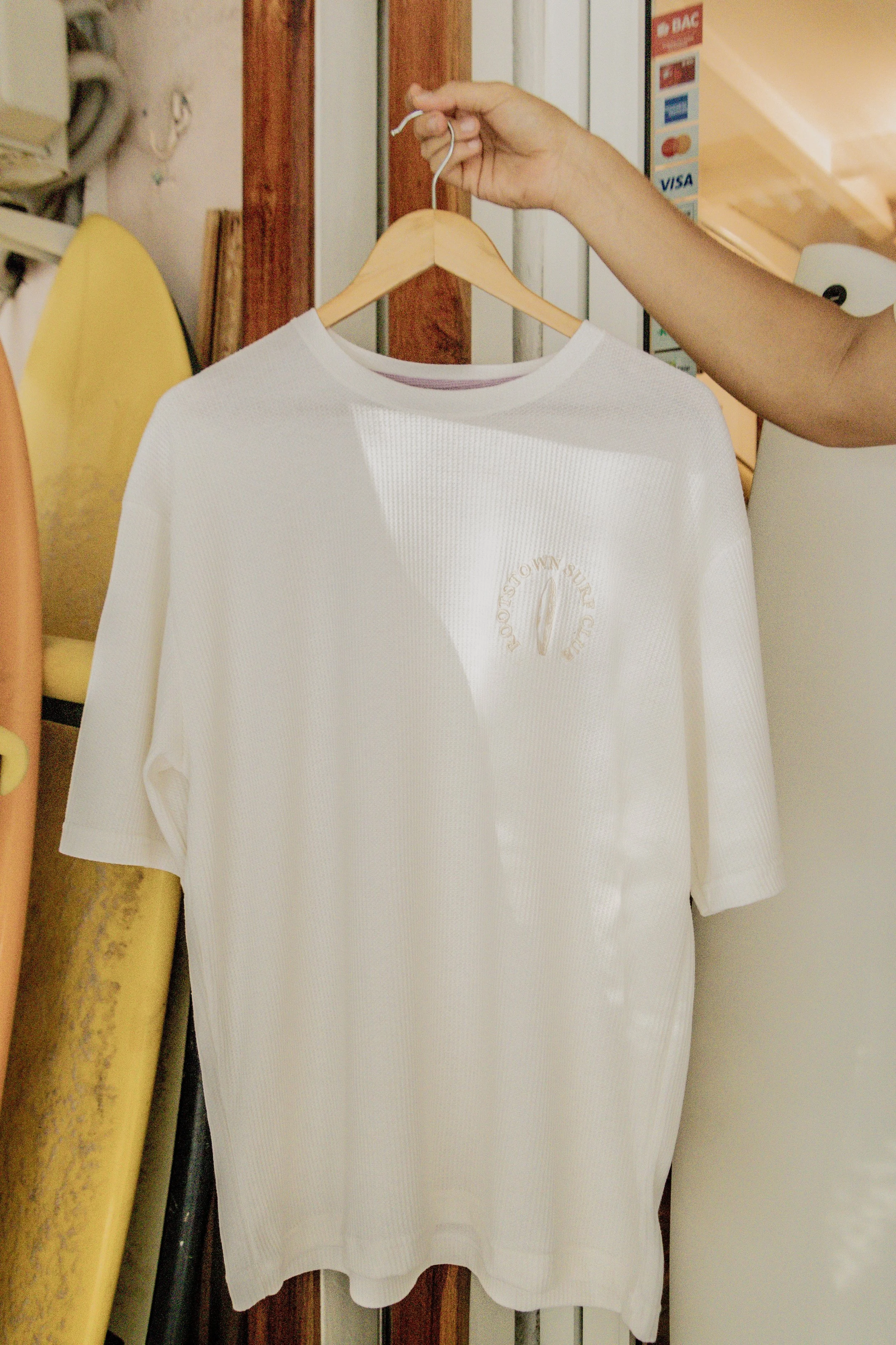 A white T-shirt displayed on a wooden hanger, being held by a person's hand.
