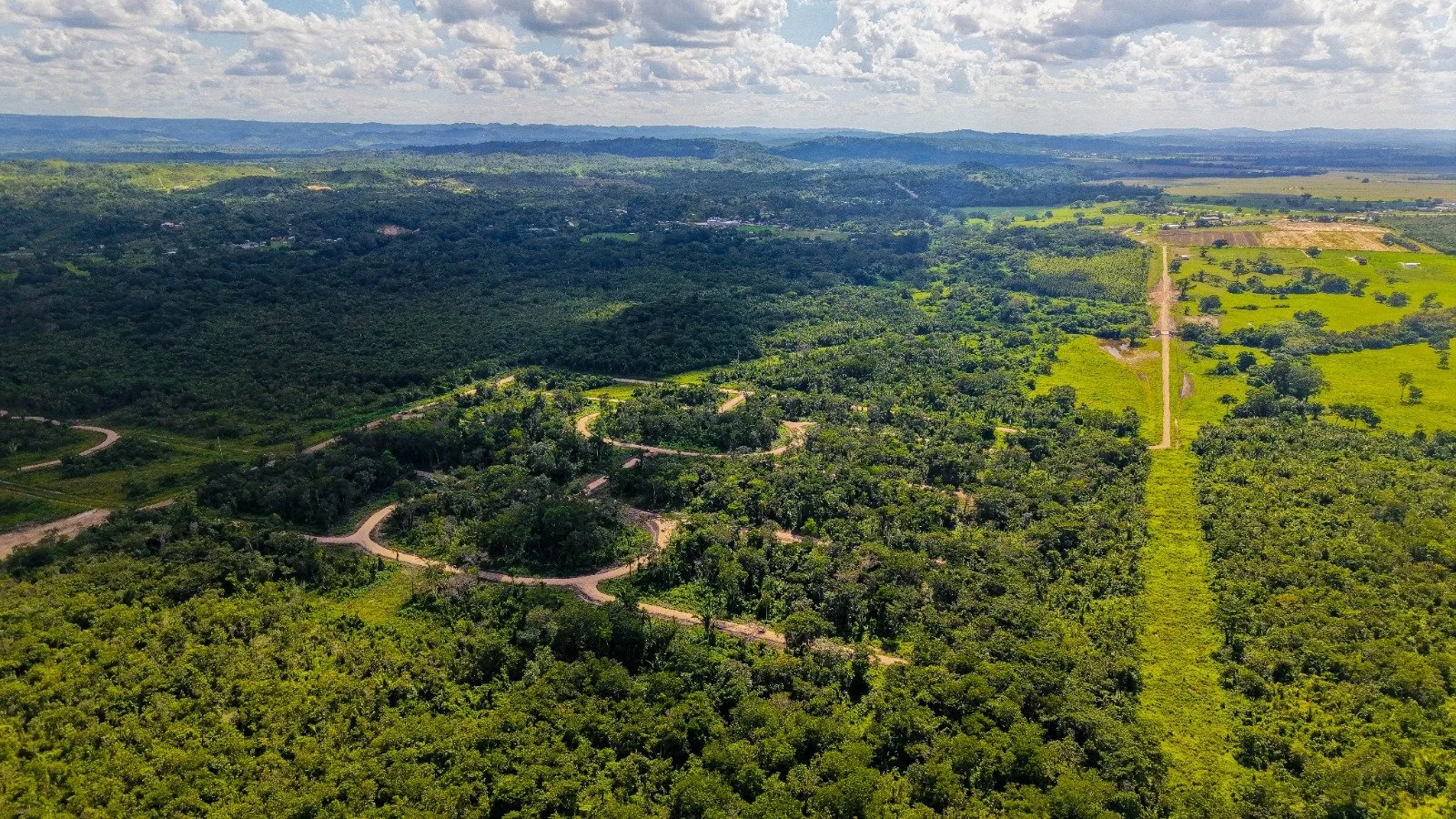 Aerial view of a rural landscape with forests, fields, and winding roads under a partly cloudy sky.