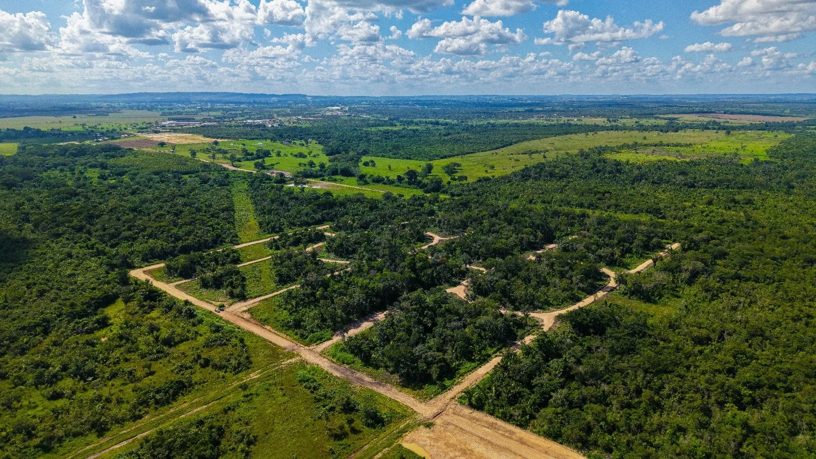 Aerial view of a green landscape with roads, trees, and open fields under a partly cloudy sky.