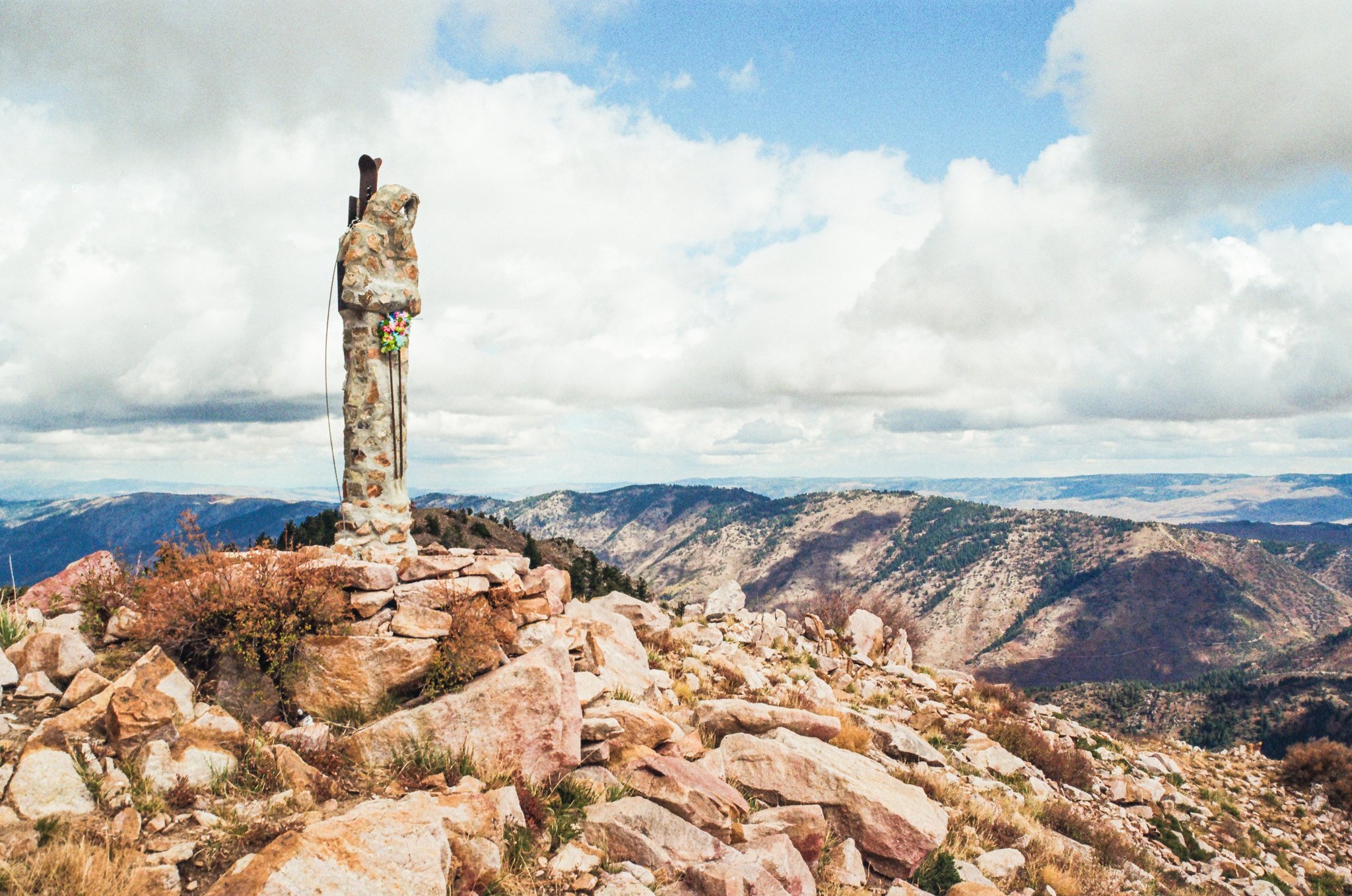 A stone monument on a rocky mountain top with a view of distant mountain ranges under cloudy sky.