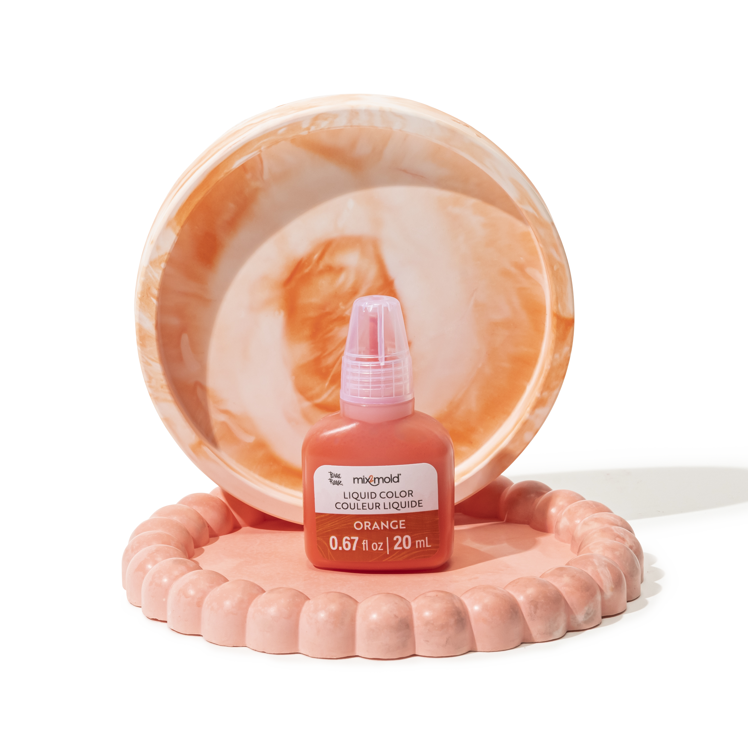 A container of orange liquid color dye with a label indicating it is orange, placed on a pink beaded circular base, with an orange marble pattern dish behind it.