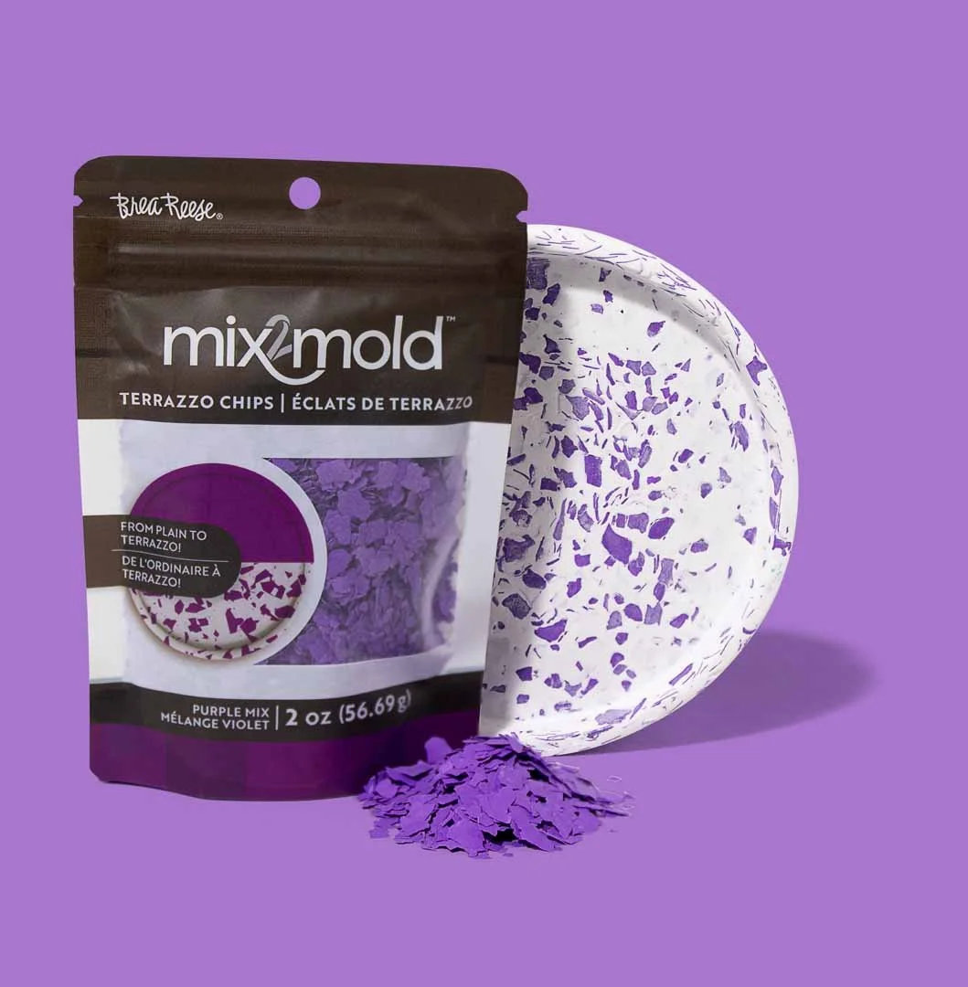 A package of Mix2Mold Terrazzo Chips in purple mix color, with some chipped material spilled in front, and a white plate with purple and white terrazzo pattern, all set against a purple background.