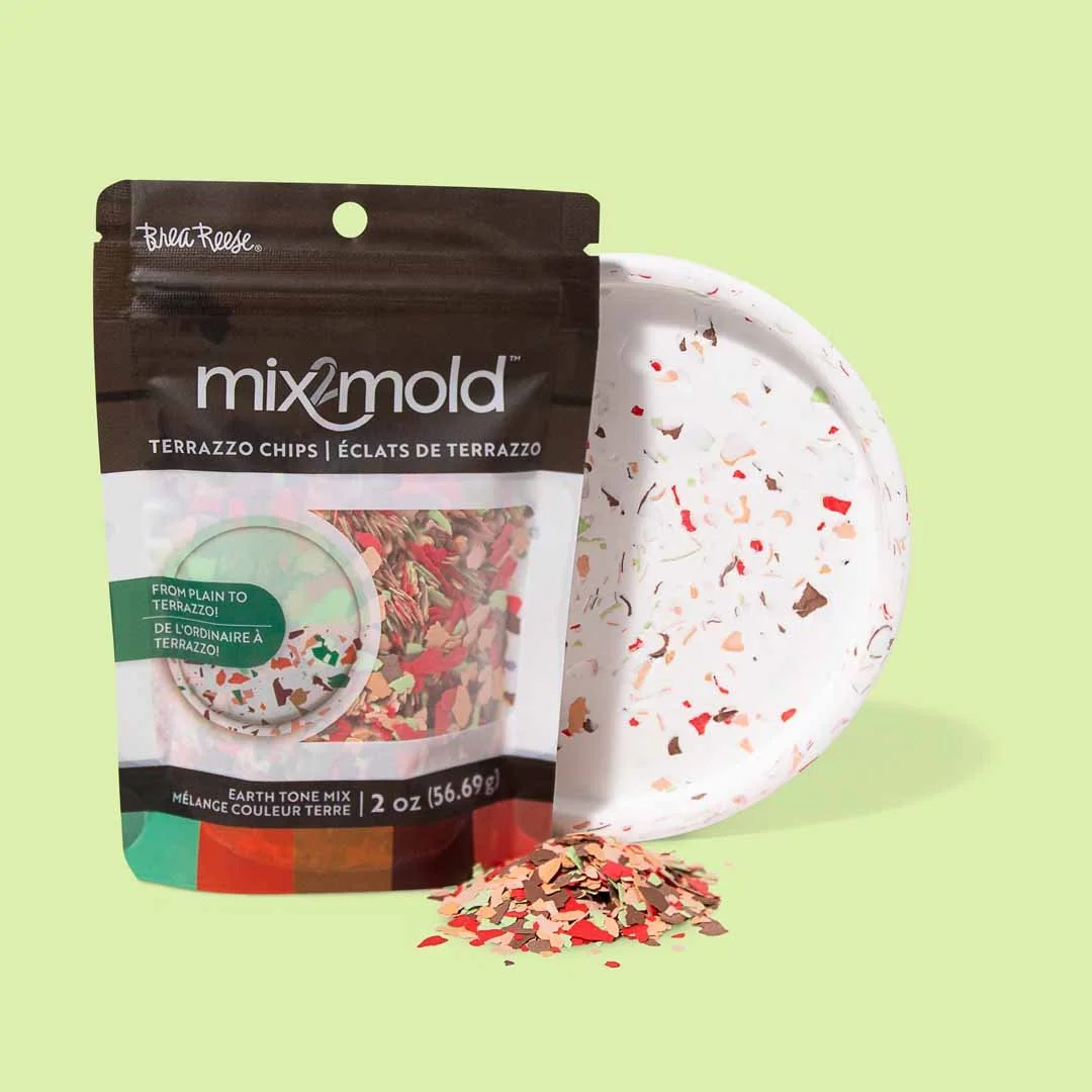 A bag of MixMold terrazzochips with colorful terrazzo chips spilling out, a terrazzo plate behind them with more chips, all set against a light green background.