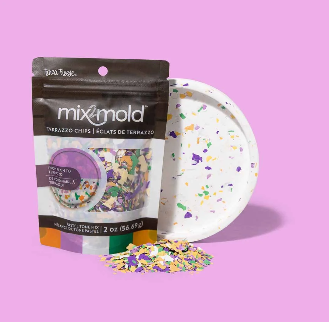 A package of Mix2mold terrazzo chips with colorful pieces, a terrazzo plate in the background, and some loose chips in front on a purple surface.