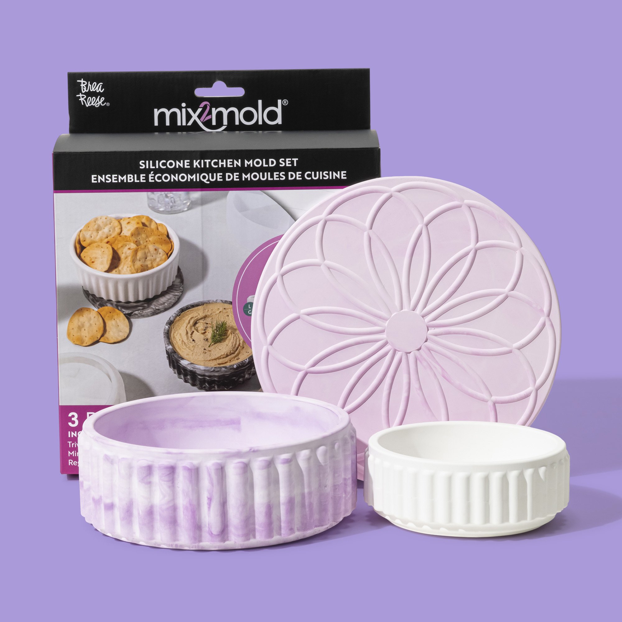 A silicone kitchen mold set includes a large pink flower-shaped mold, a purple marble-textured round mold, and a white ribbed round mold, placed in front of its packaging box with a lavender background.