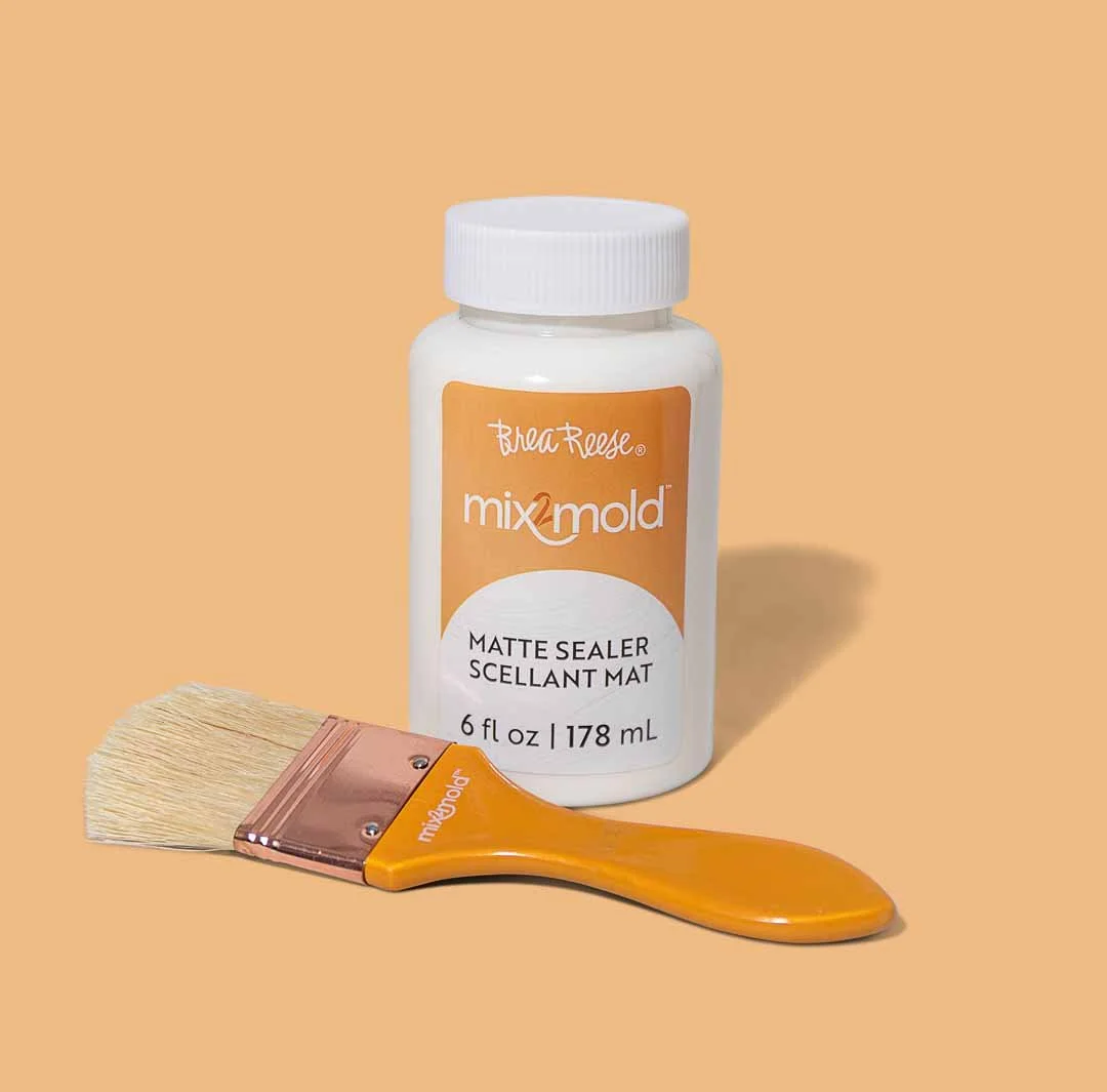 A bottle of mix mold matte sealer and a paintbrush on a beige background.