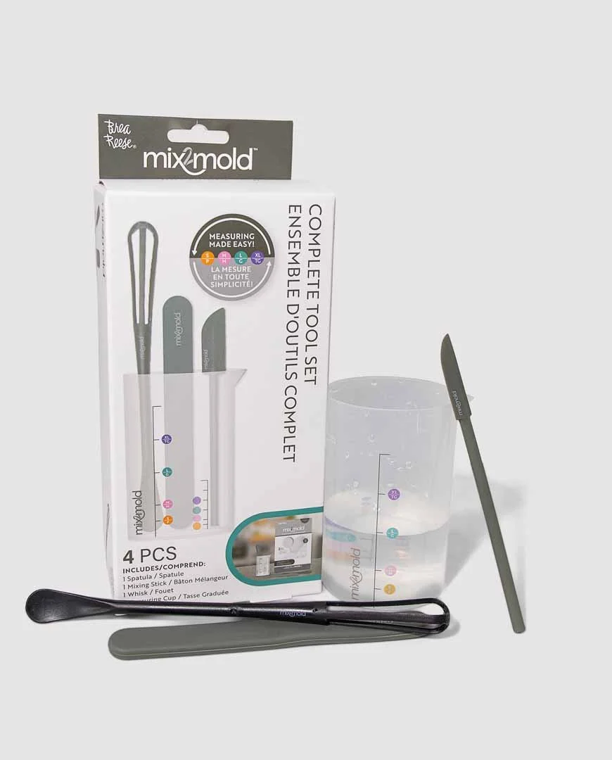 A boxed MixMold complete tool set with a spatula, mixing stick, and whisk, along with a measuring cup and utensils outside the box, on a white background.