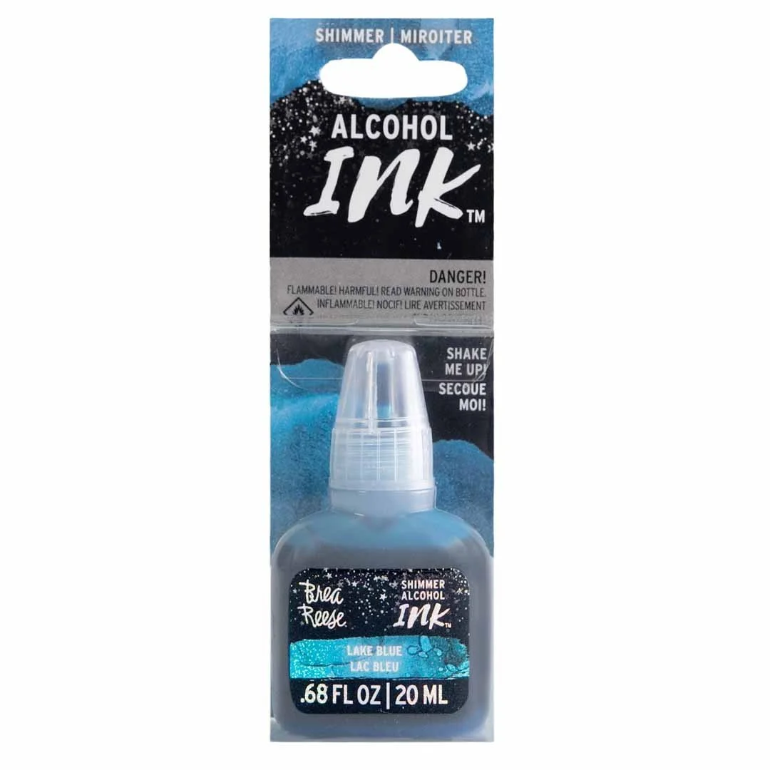 A small bottle of shimmer alcohol ink in lake blue color with a clear cap, packaged in a blister pack with black, blue, and white design, labeled for hobby or craft use.