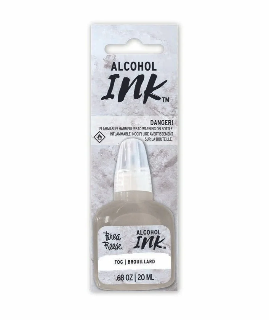 A small bottle of alcohol ink labeled 'Brea Reese' in a plastic package with a cardboard backing. The ink color is fog or brouillard, and the bottle contains 0.68 ounces (20 milliliters). The packaging warns that the ink is flammable.