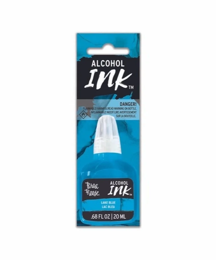 A small bottle of alcohol ink labeled 'Lake Blue' with warning labels and packaging.