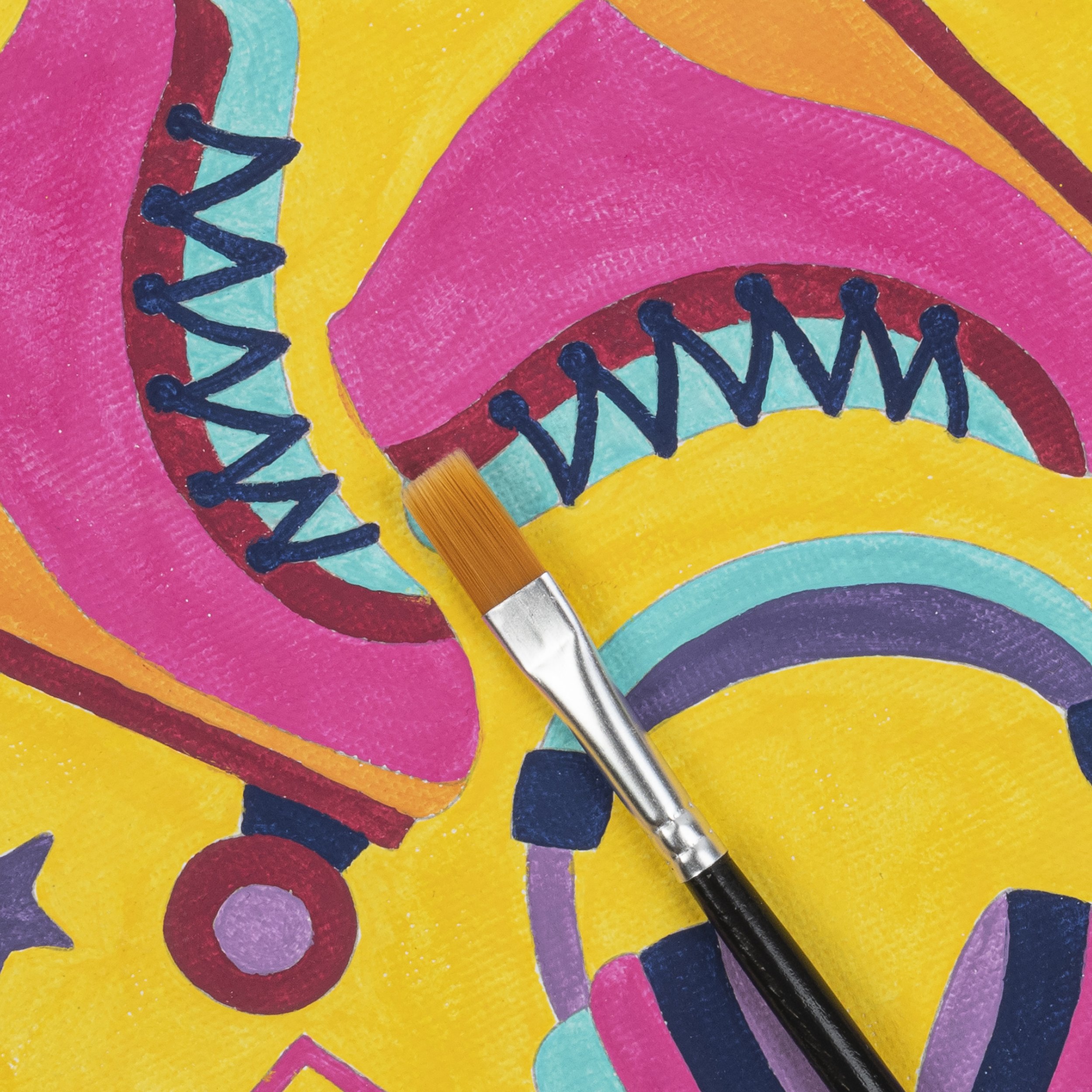 Close-up of a colorful, abstract painting with a small paintbrush resting on it. The painting features bright pink, yellow, orange, teal, purple, and blue shapes with black outlines and patterns.