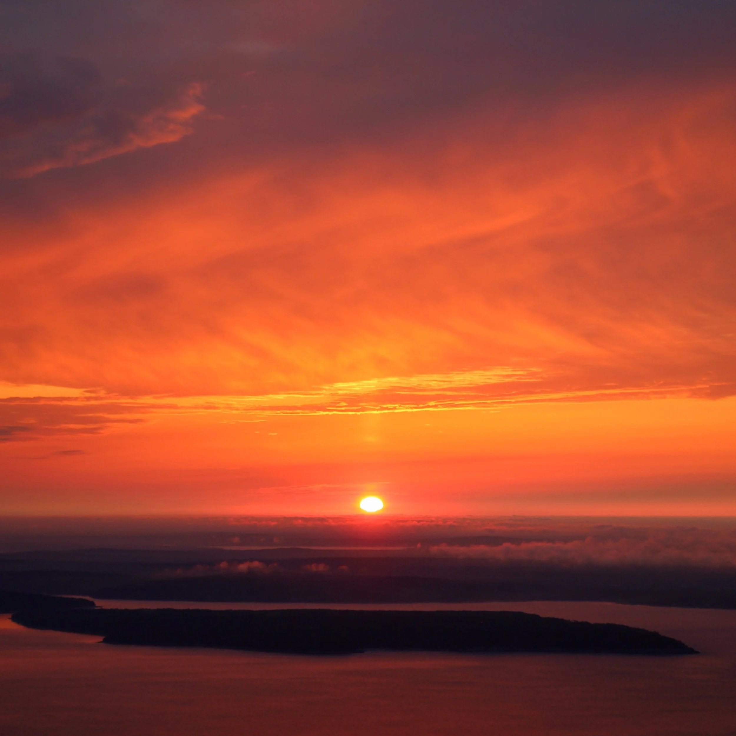 Sunset over a body of water with colorful pink, orange, and purple clouds in the sky.