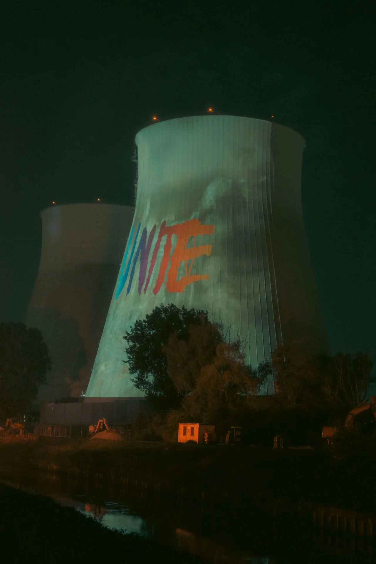 Une centrale nucléaire avec une projection lumineuse multicolore sur ses tours, le tout de nuit.