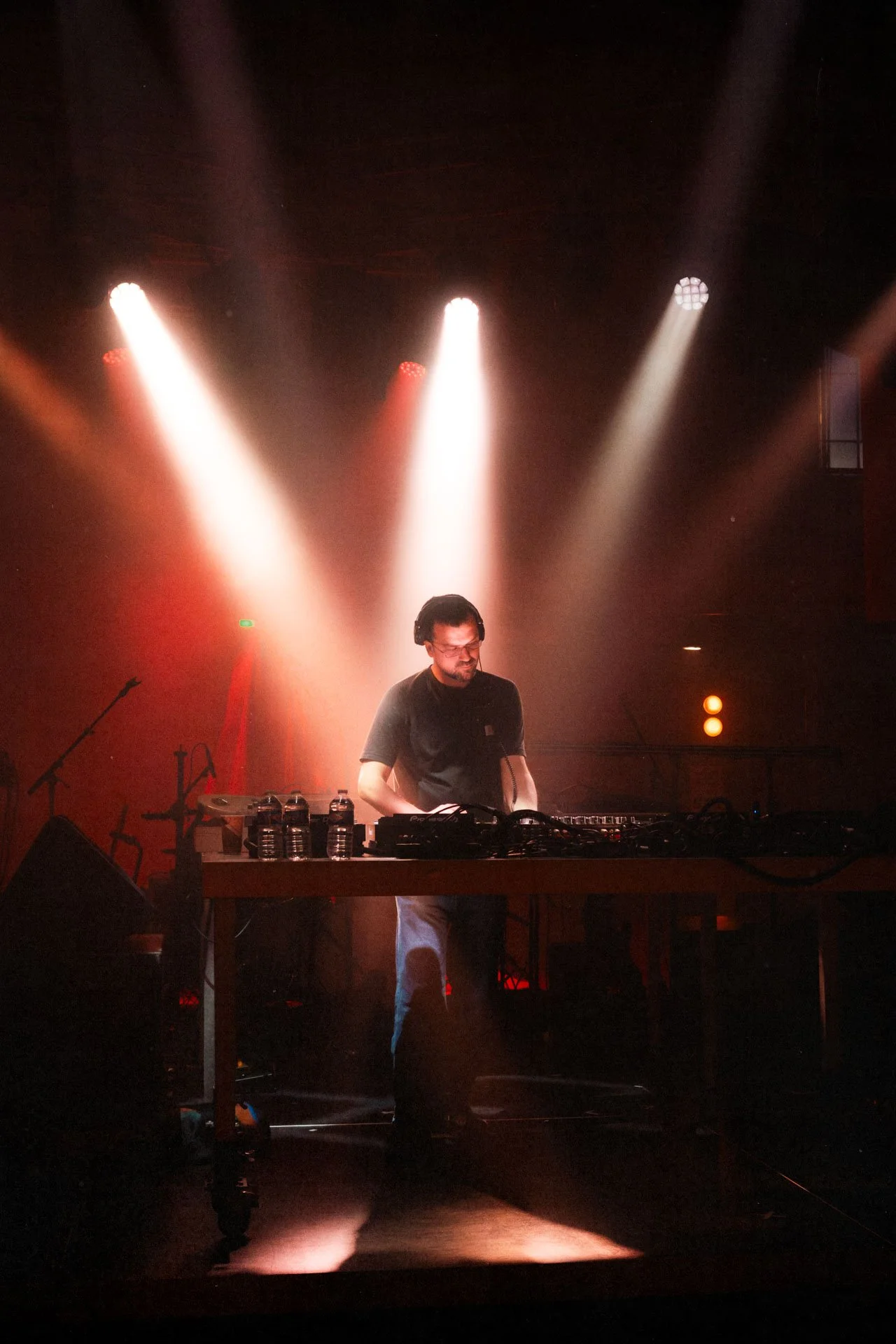 Un DJ derrière une table de mixage sous des lumières de scène rouge et blanche.