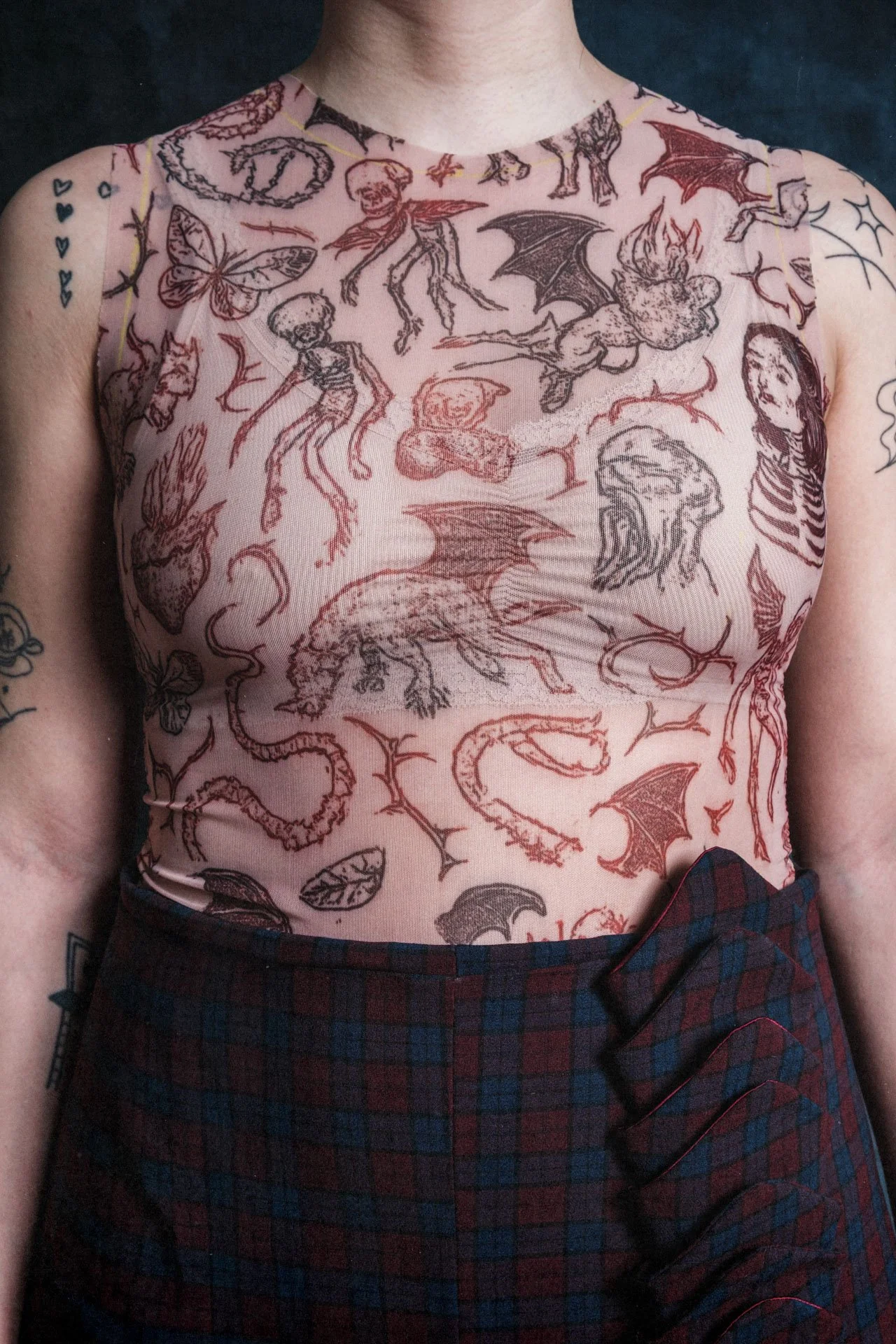 Un haut en tissu transparent avec un motif de dessins de créatures fantastiques, comme des dragons, des squelettes et des démons, porté par une personne