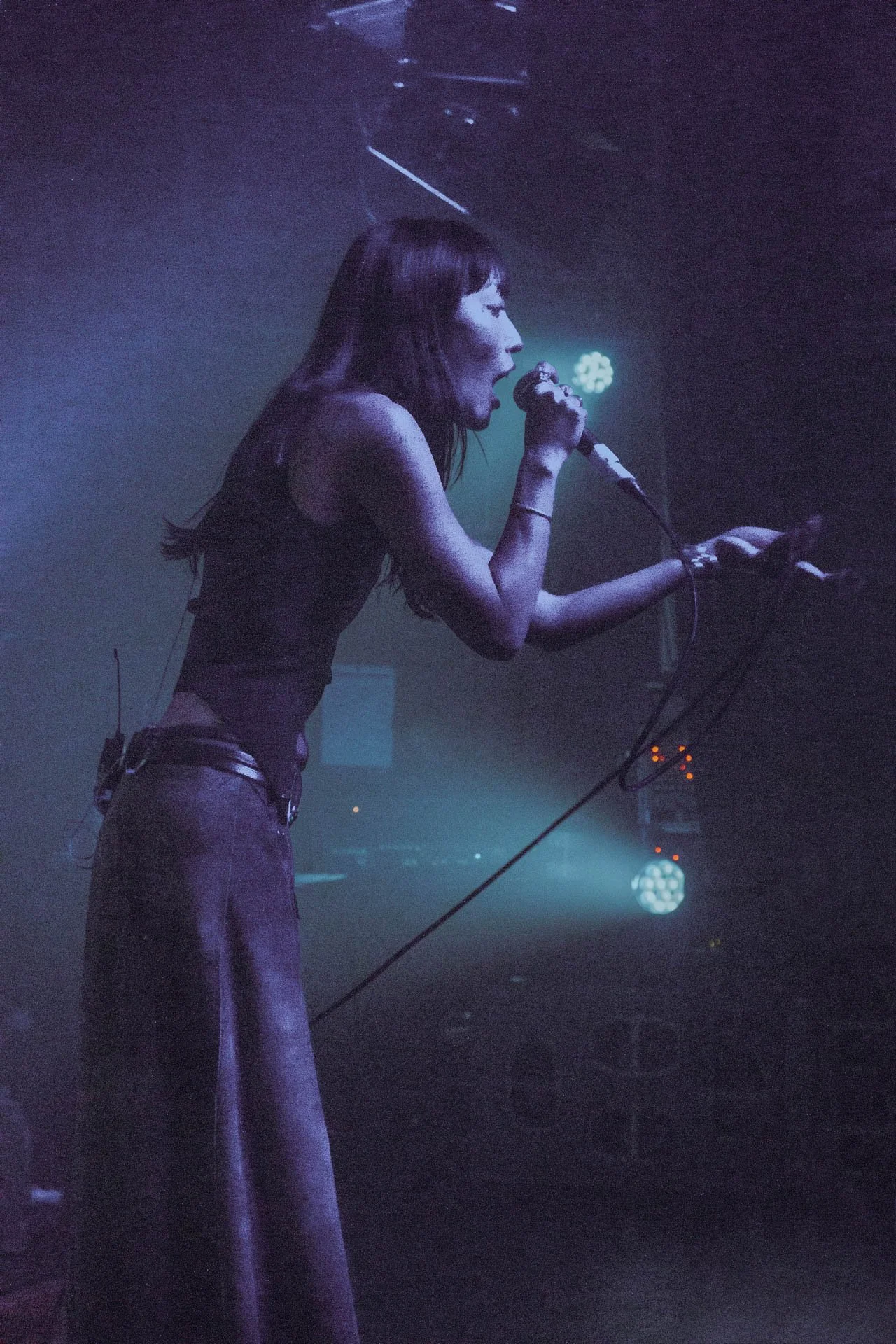 Une femme chante dans un contexte de scène ou de concert, tenant un micro et utilisant un appareil électronique ou une console de mixage.