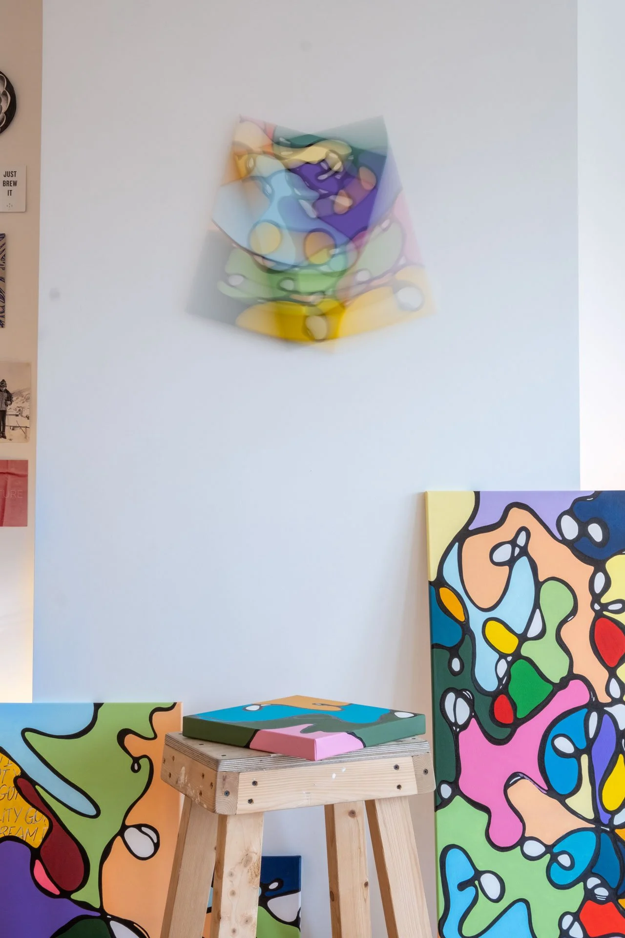 Une œuvre d'art abstraite colorée avec des formes fluides, exposée dans une galerie. Des peintures colorées avec des motifs similaires sont visibles dans l'image.