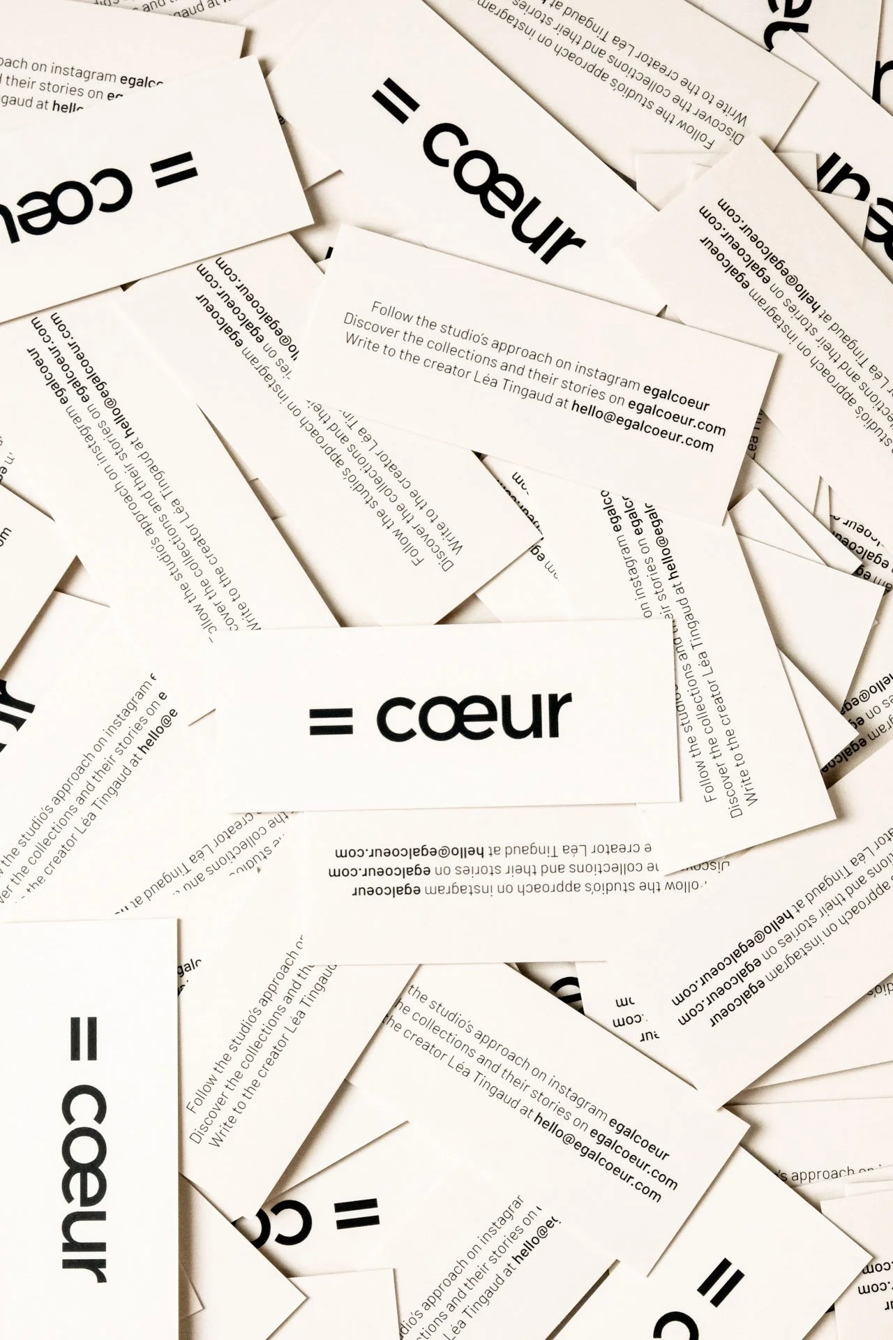 Un tas de cartes de visite blanches avec le logo '=' et le mot 'coeur' en style moderne. Certaines cartes contiennent du texte en anglais concernant une approche créative sur Instagram et un contact email.