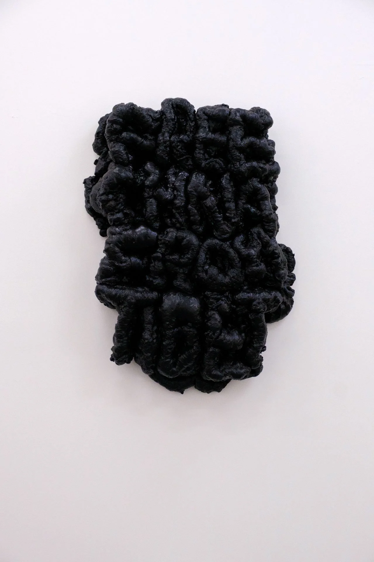Image d'une pierre noire en forme rectangulaire avec une surface texturée et irrégulière, placée sur un fond blanc.