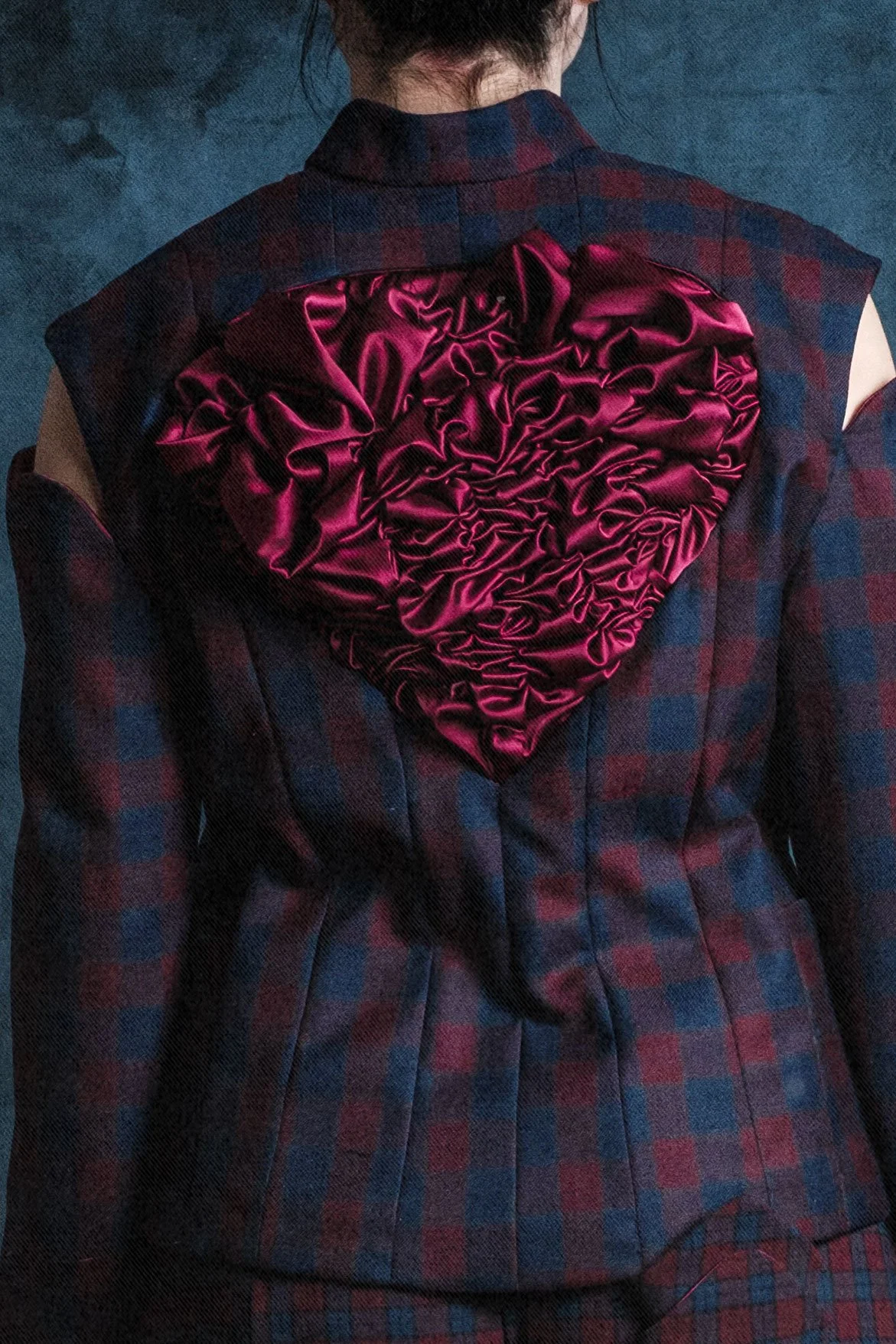 Une personne portant une veste à carreaux rouges et bleus, avec un grand cœur en satin rose fusionné dans le dos.