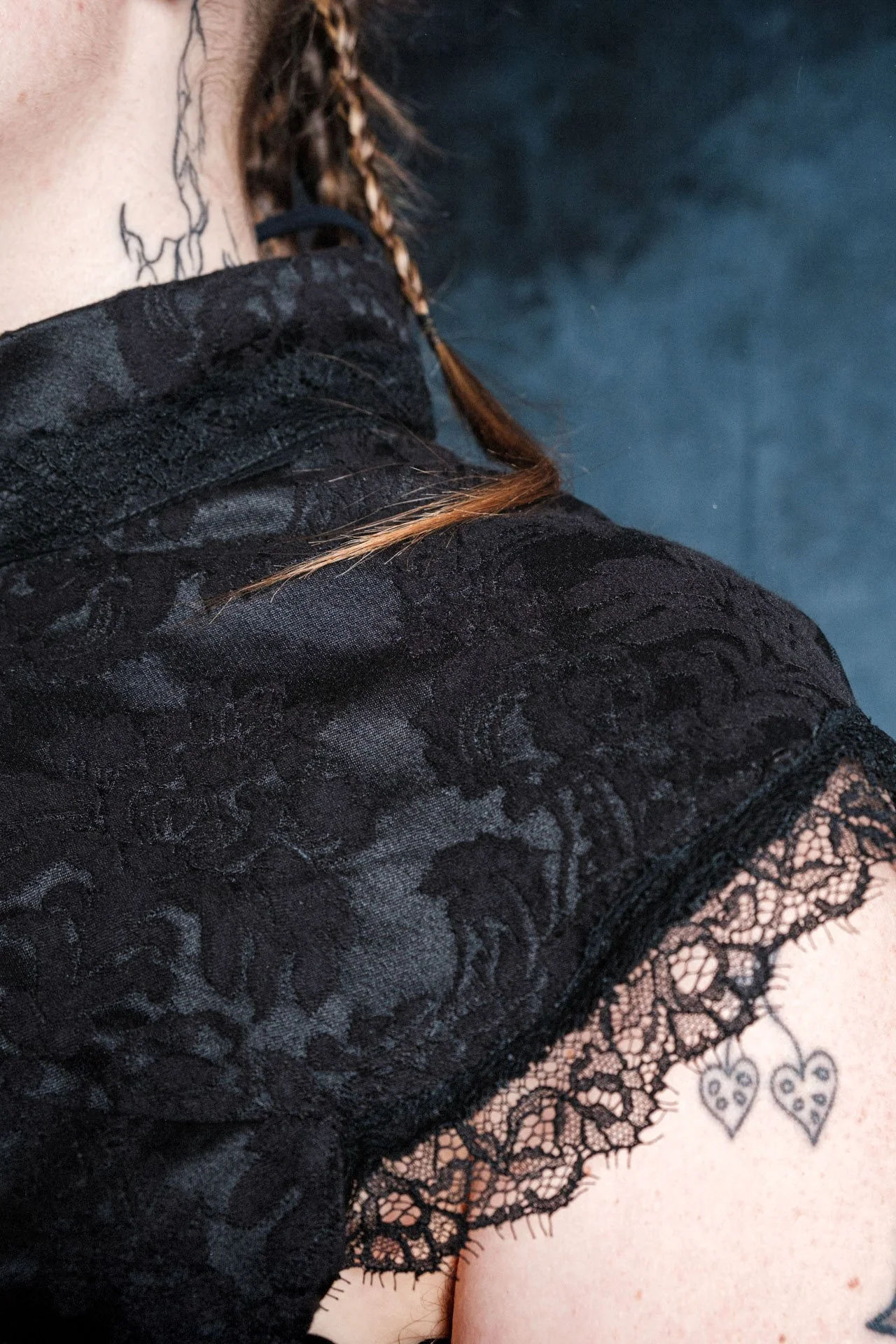 Zoom sur une robe en dentelle noire avec un motif floral et une bordure en dentelle, portée par une personne dont une partie de l'épaule est visible.