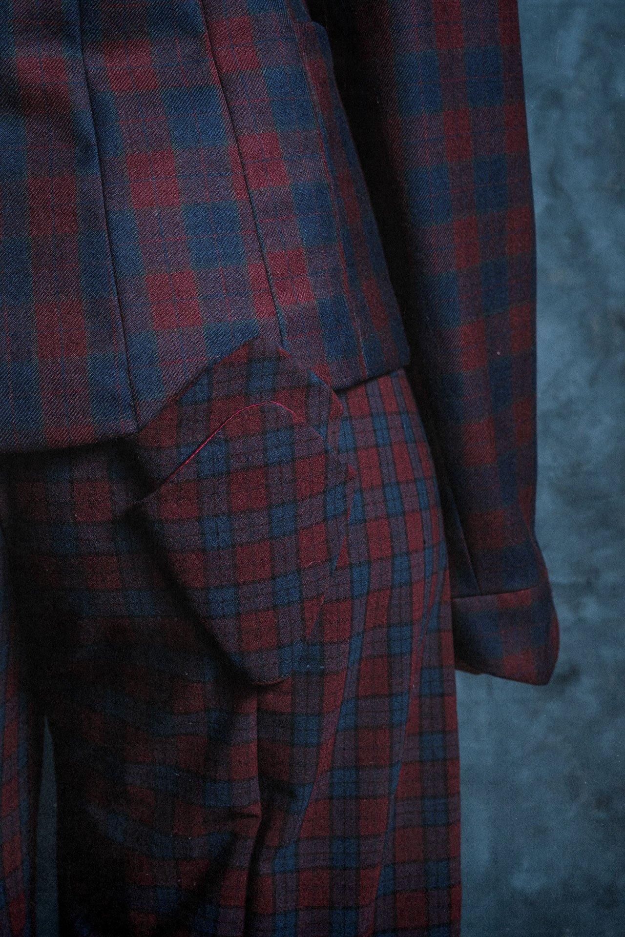 Vêtement en tartan rouge, bleu foncé et noir. La photo met en valeur le tissu d'un costume ou d'un blazer. L'arrière-plan est flou et sombre.