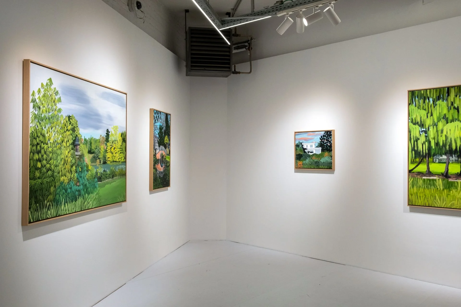 Quatre peintures représentant des paysages verdoyants dans une galerie d'art