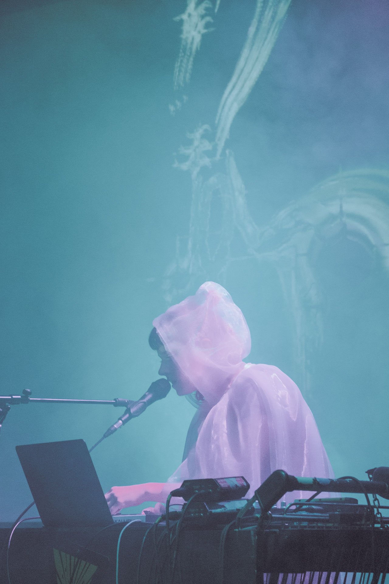 Musicien en vêtements lumineux jouant du clavier et chantant avec un micro, devant un fond coloré avec projection d'images.