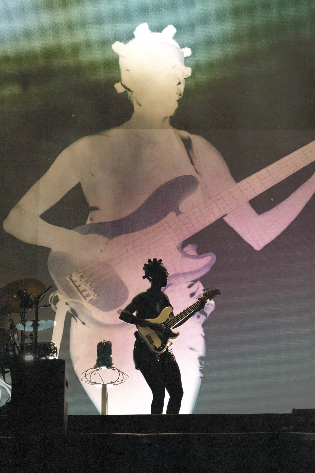 Une scène de concert avec un musicien jouant de la guitare électrique sur scène, avec une grande projection en arrière-plan montrant une image stylisée d'une femme jouant de la guitare et portant un chignon.