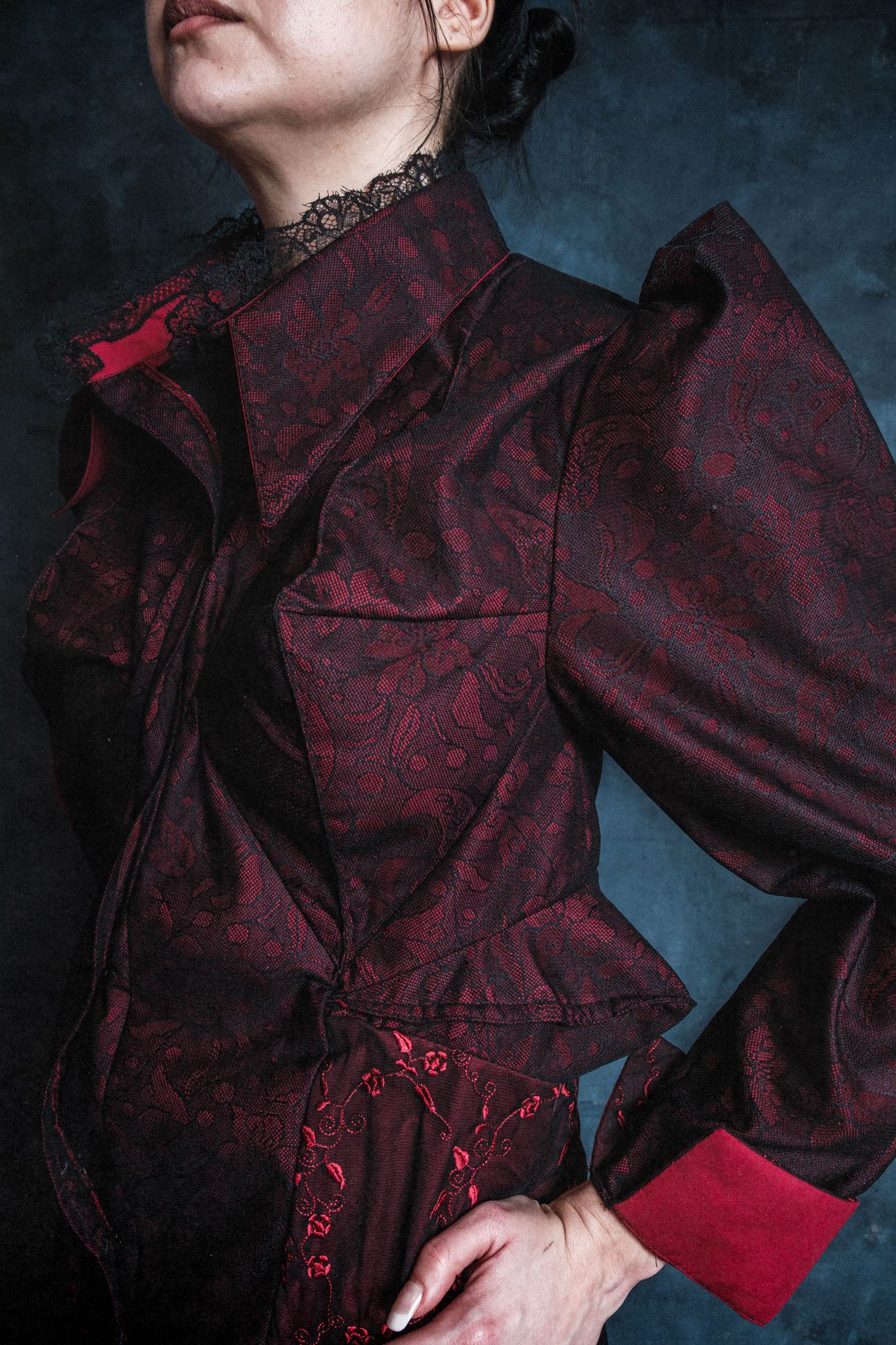 Une femme porte une veste noire et rouge avec un motif floral brodé, un col en dentelle noire et une manche rouge avec un poignet rouge.