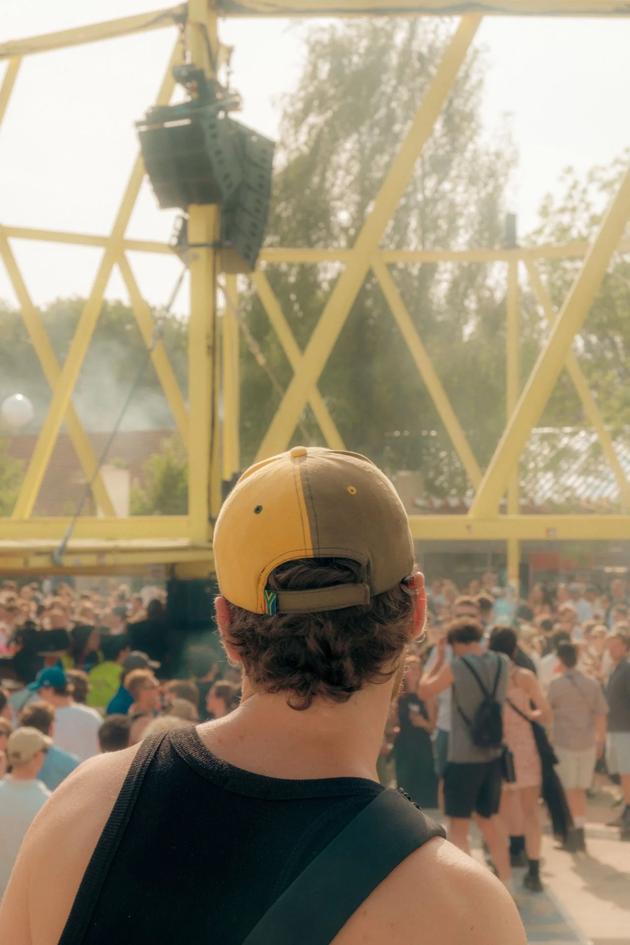 Vue derrière un homme avec une casquette regardant un concert avec une grande scène et une foule nombreuse.