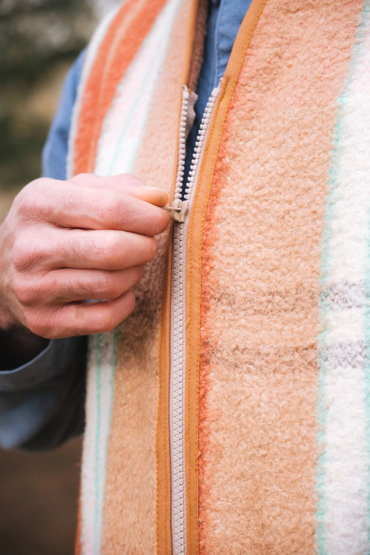 Une personne qui ouvre une fermeture éclair sur une veste ou un manteau orange en laine, avec des accents de couleur blanche, turquoise et beige.