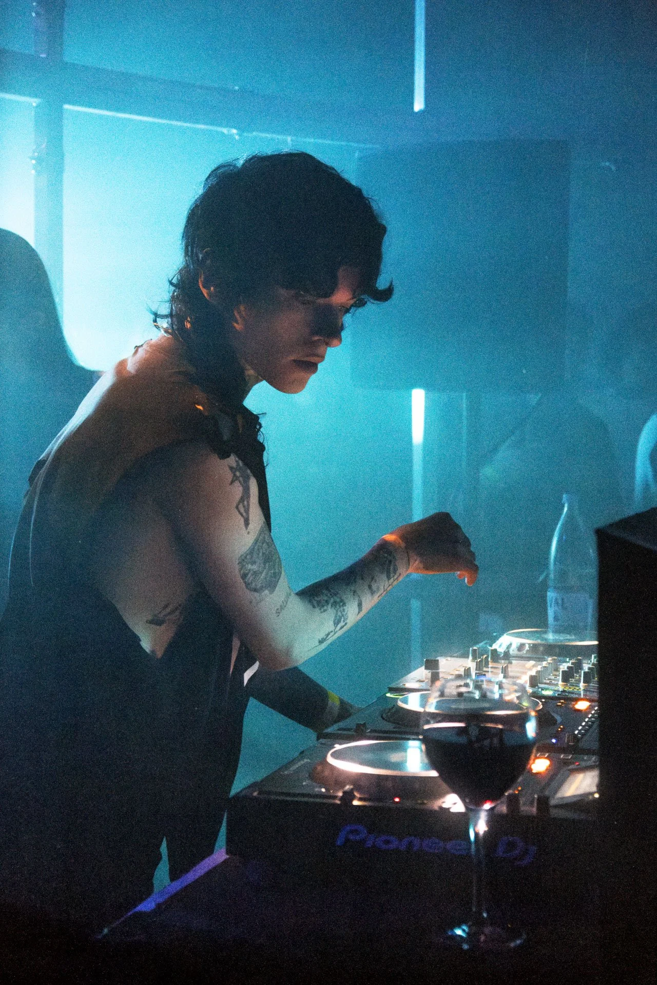 Un DJ avec des tatouages joue à la console dans une lumière bleue, ambiance de club