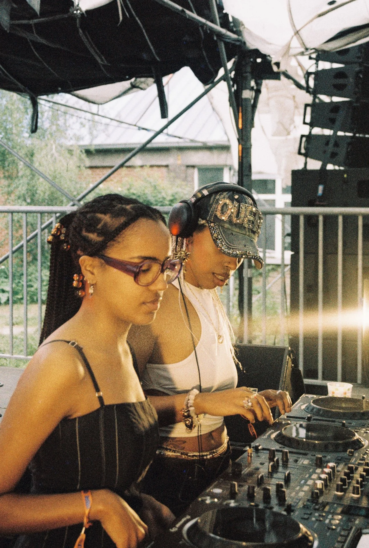 Deux femmes DJ en train de mixer de la musique lors d'un événement en extérieur, avec du matériel DJ et un espace en plein air en arrière-plan.