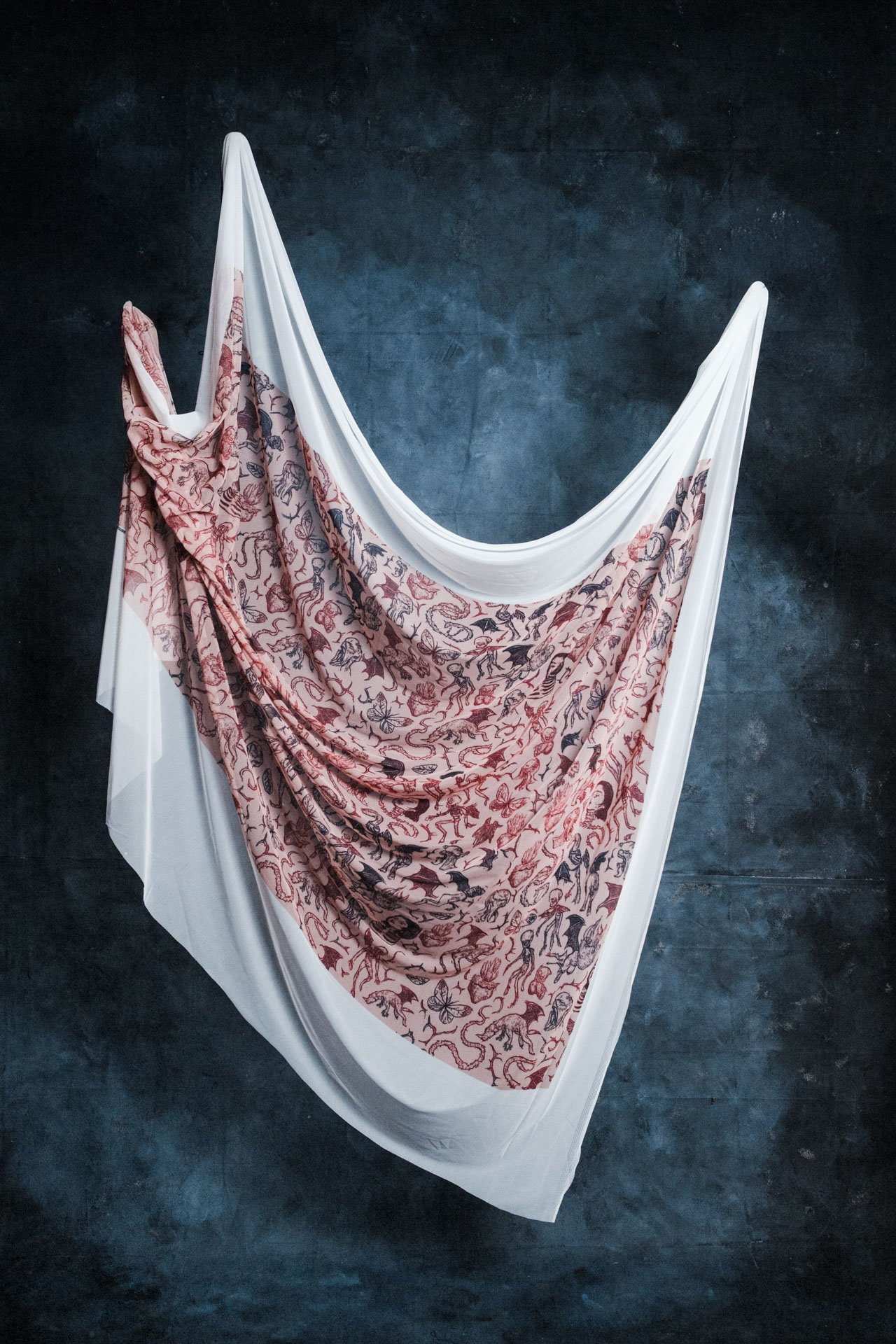 Une œuvre d'art composée d'une toile blanche tendue sur une structure en forme de pont, avec une draperie aux motifs d'animaux et de fleurs en rouge et noir suspendue au centre, le tout placé contre un mur noir.