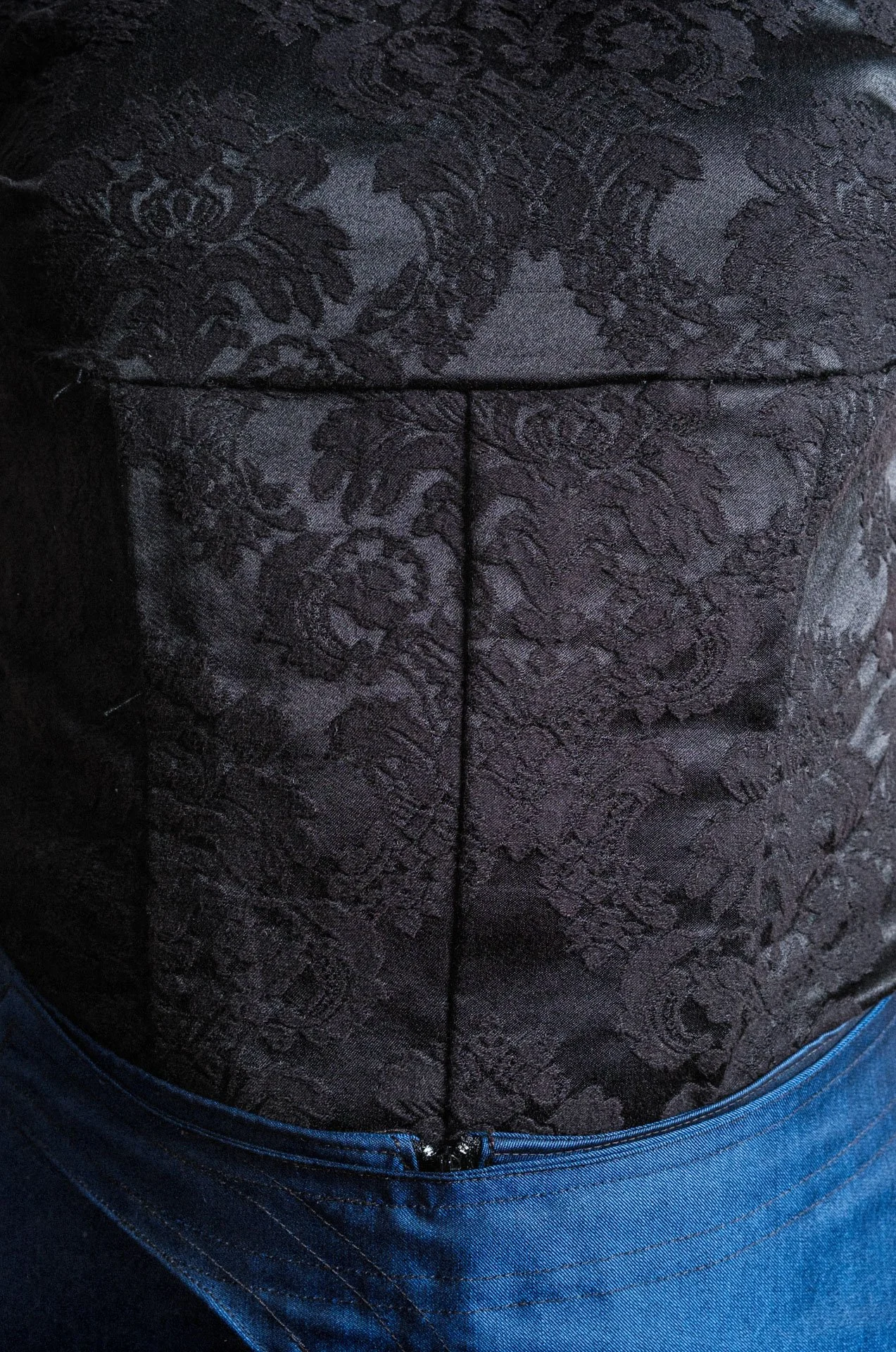 Veste noire en tissu jacquard avec motif floral gravé, zippée à la taille.