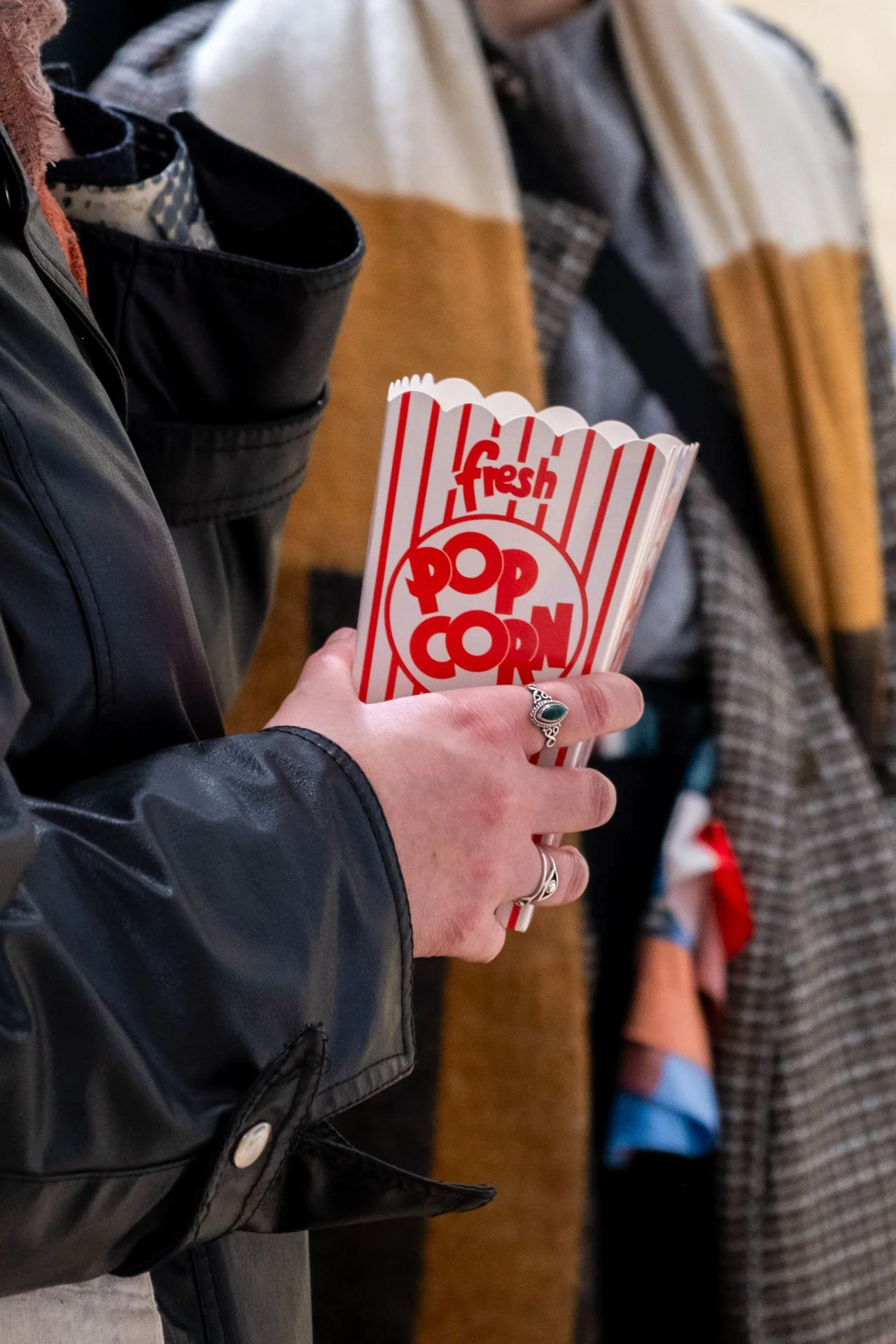 Une personne tenant un seau de popcorn rouge et blanc avec l'inscription "fresh popcorn" en rouge.