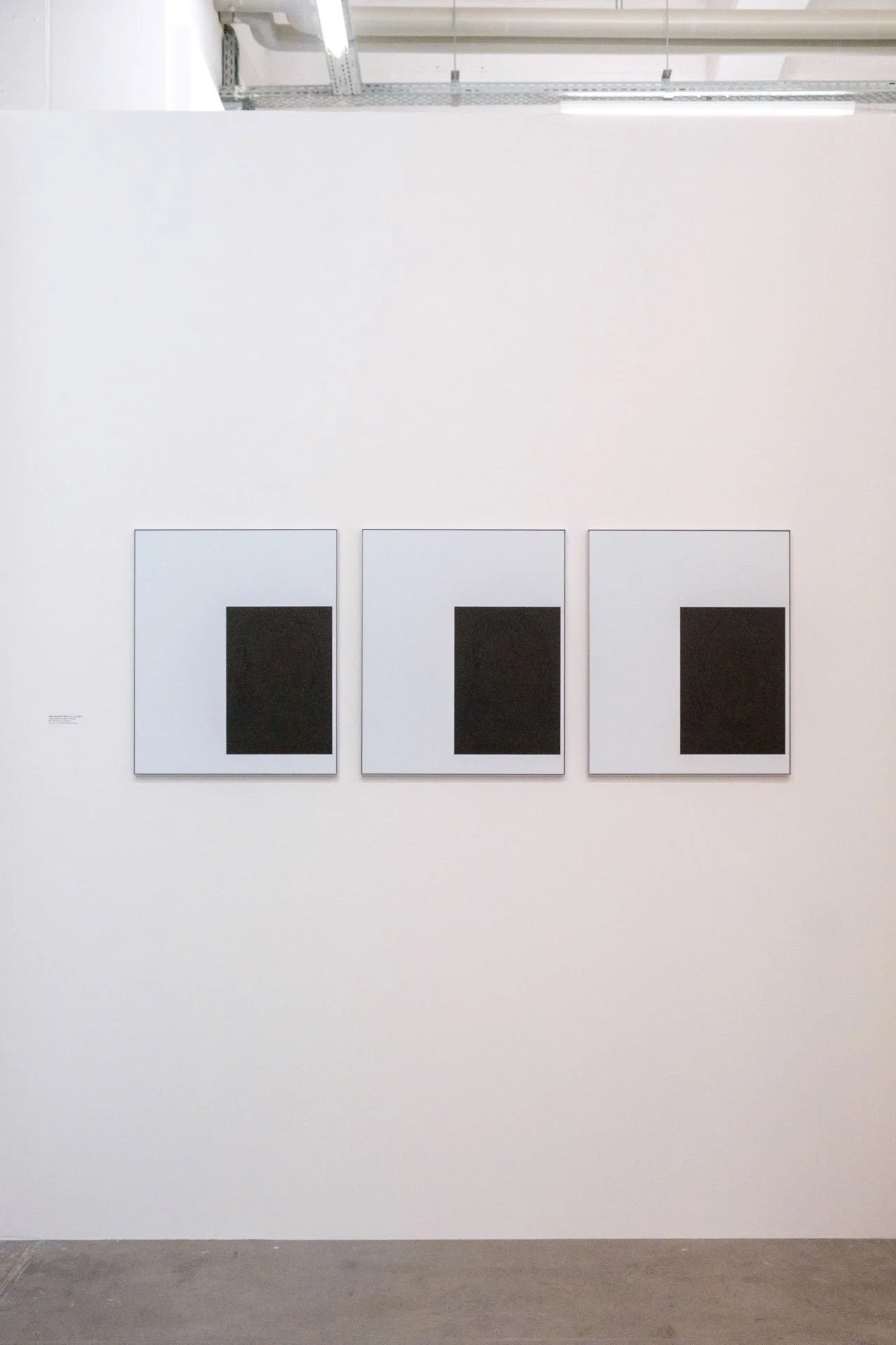 Trois œuvres d'art abstraites avec des formes rectangulaires noires sur fond blanc, exposées au mur dans une galerie.