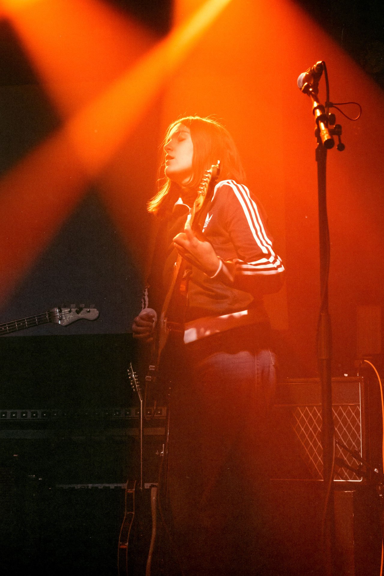 Une femme joue de la guitare sur scène, entourée de lumières orange, avec un microphone à proximité.