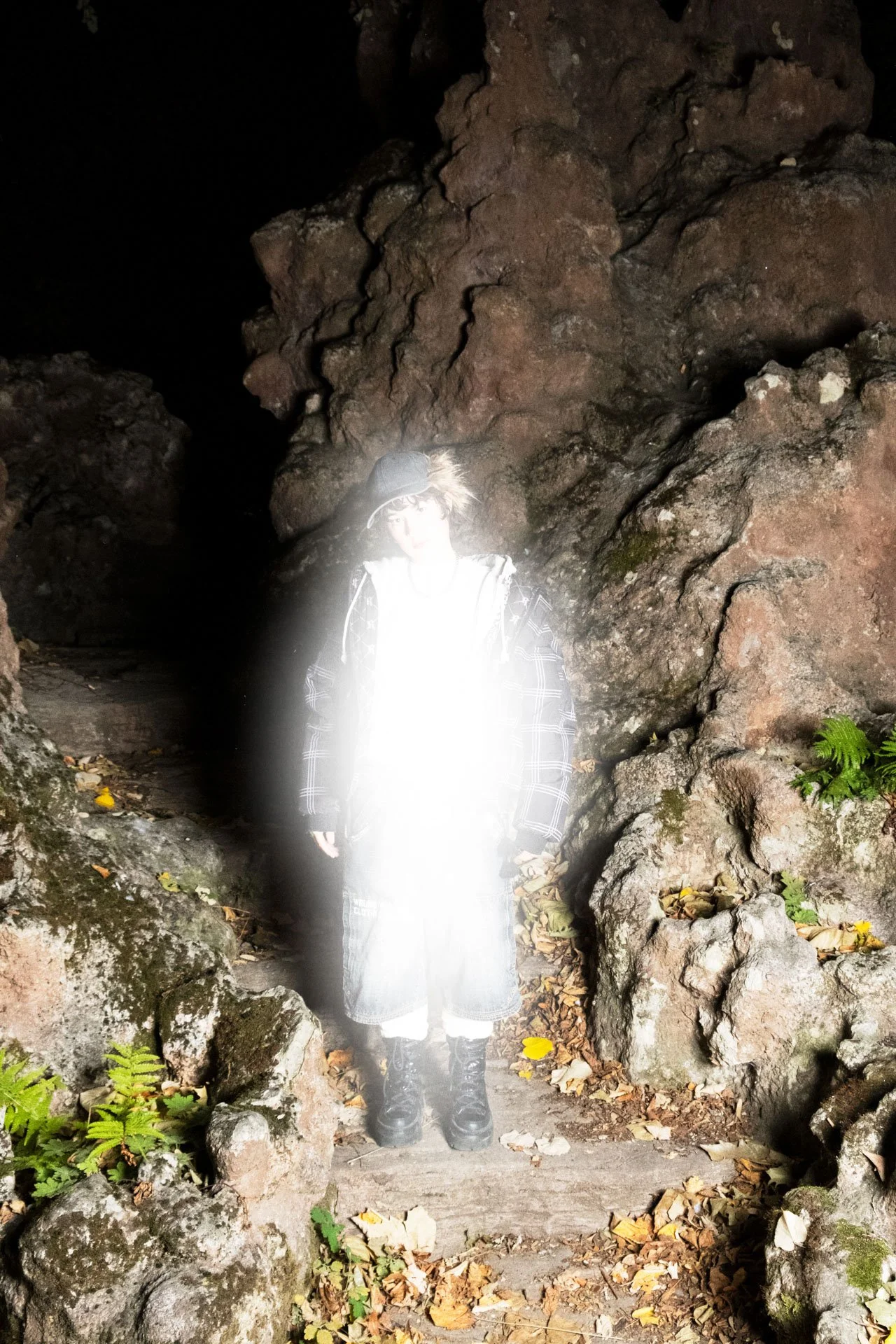 Personne dans une grotte, portant un chapeau, une veste à carreaux, et des bottes, devant une paroi rocheuse