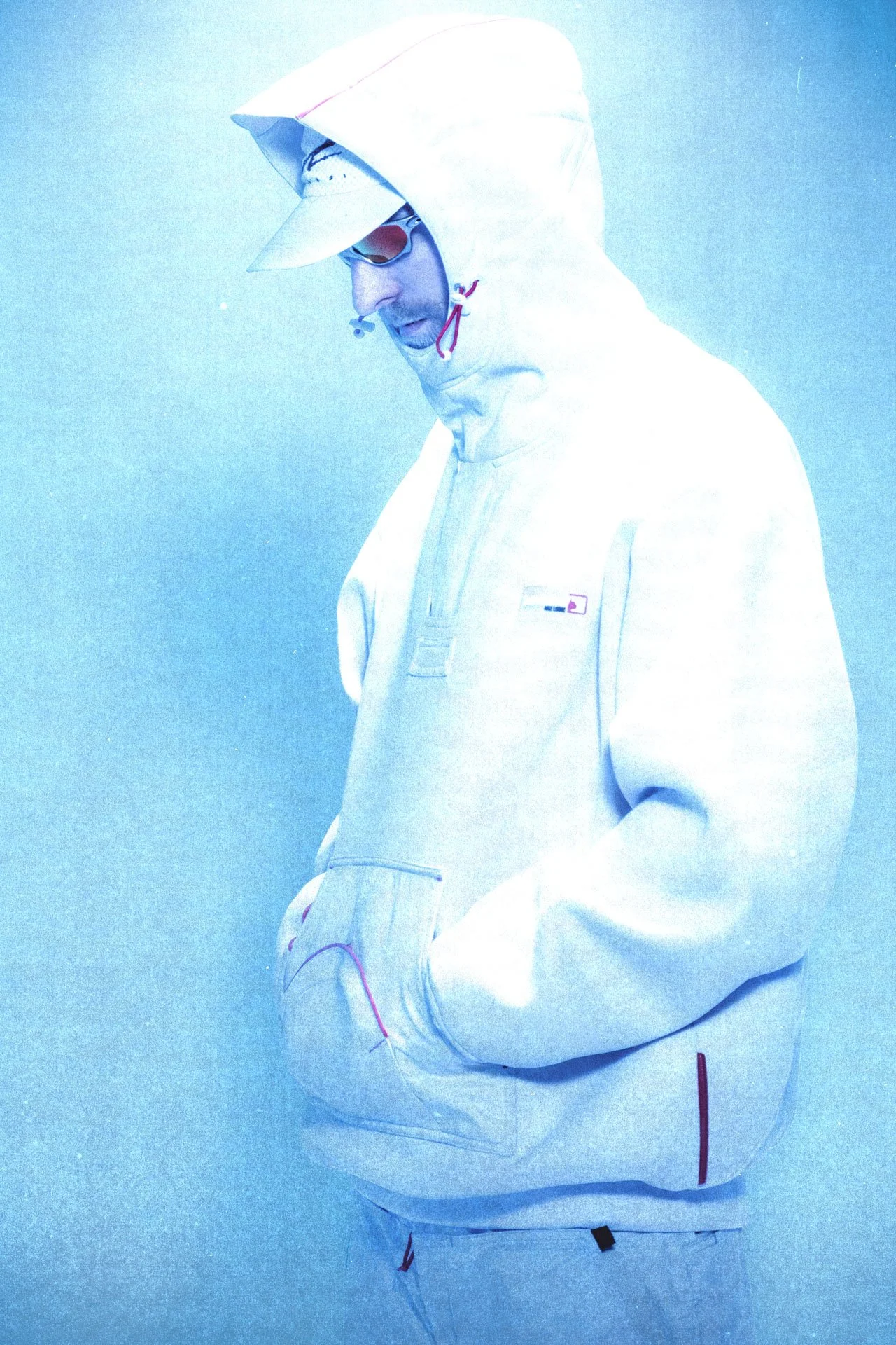 Une personne porte des vêtements de sport blancs avec des détails rouges. Elle porte une casquette, des lunettes de soleil et un casque de musique. La personne regarde vers le bas, avec une expression concentrée.