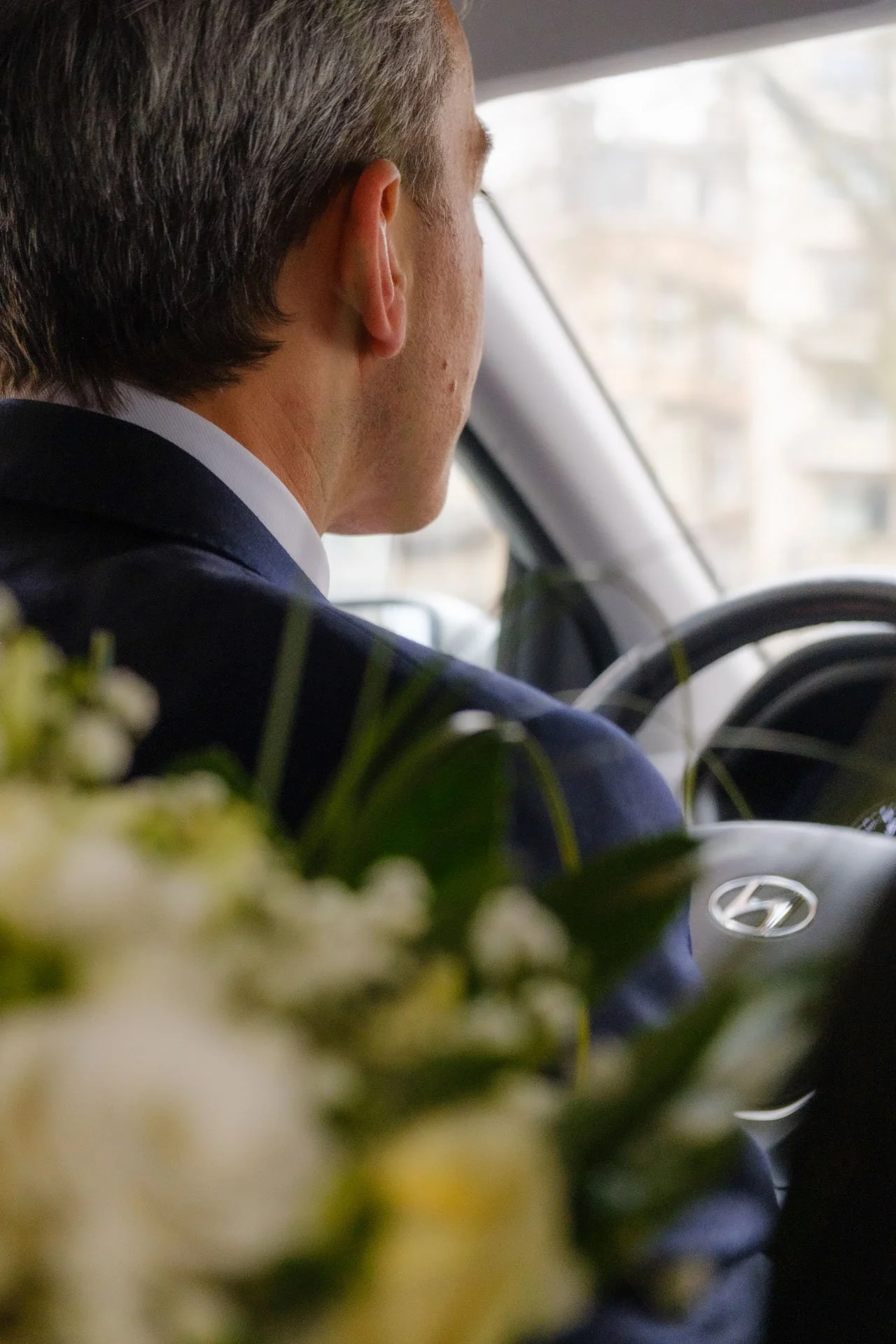 Petit garçon vu de derrière conduisant une voiture, avec des fleurs blanches et vertes devant l'objectif.