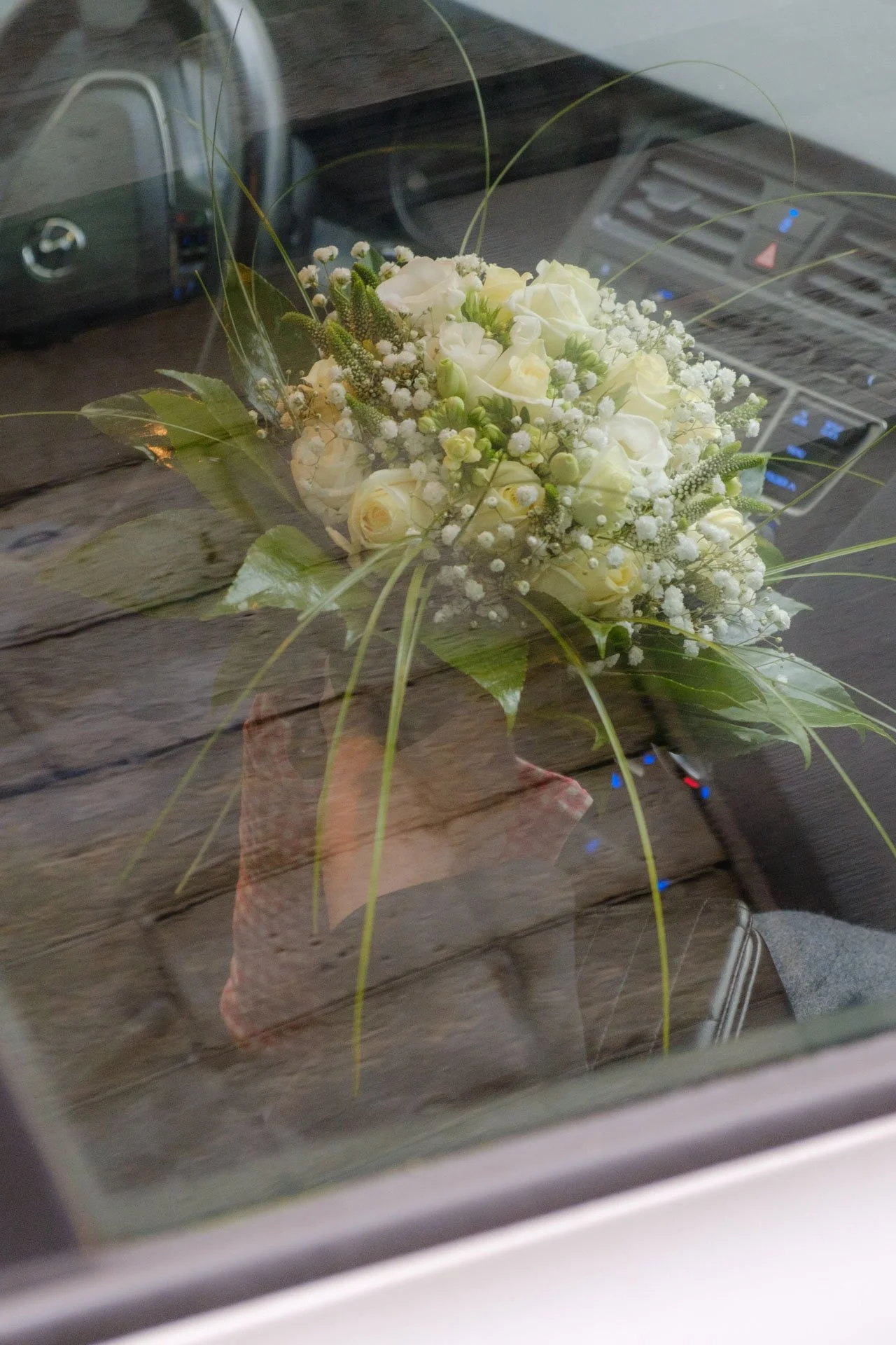 Un bouquet de fleurs blanches, dont des roses, dans un vase, placé sur une table en bois, avec un ordinateur portable et un appareil électronique en arrière-plan.