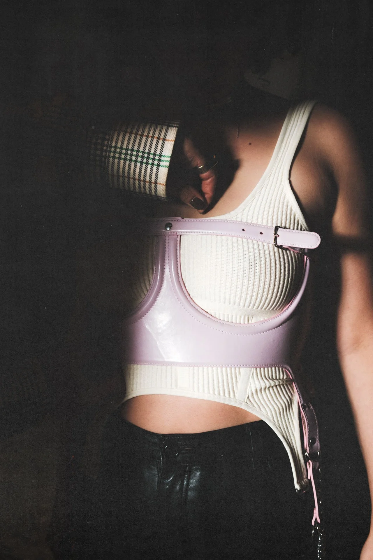 Femme portant un haut beige à rayures avec un panier rose en plastique transparent et un pantalon en cuir noir.
