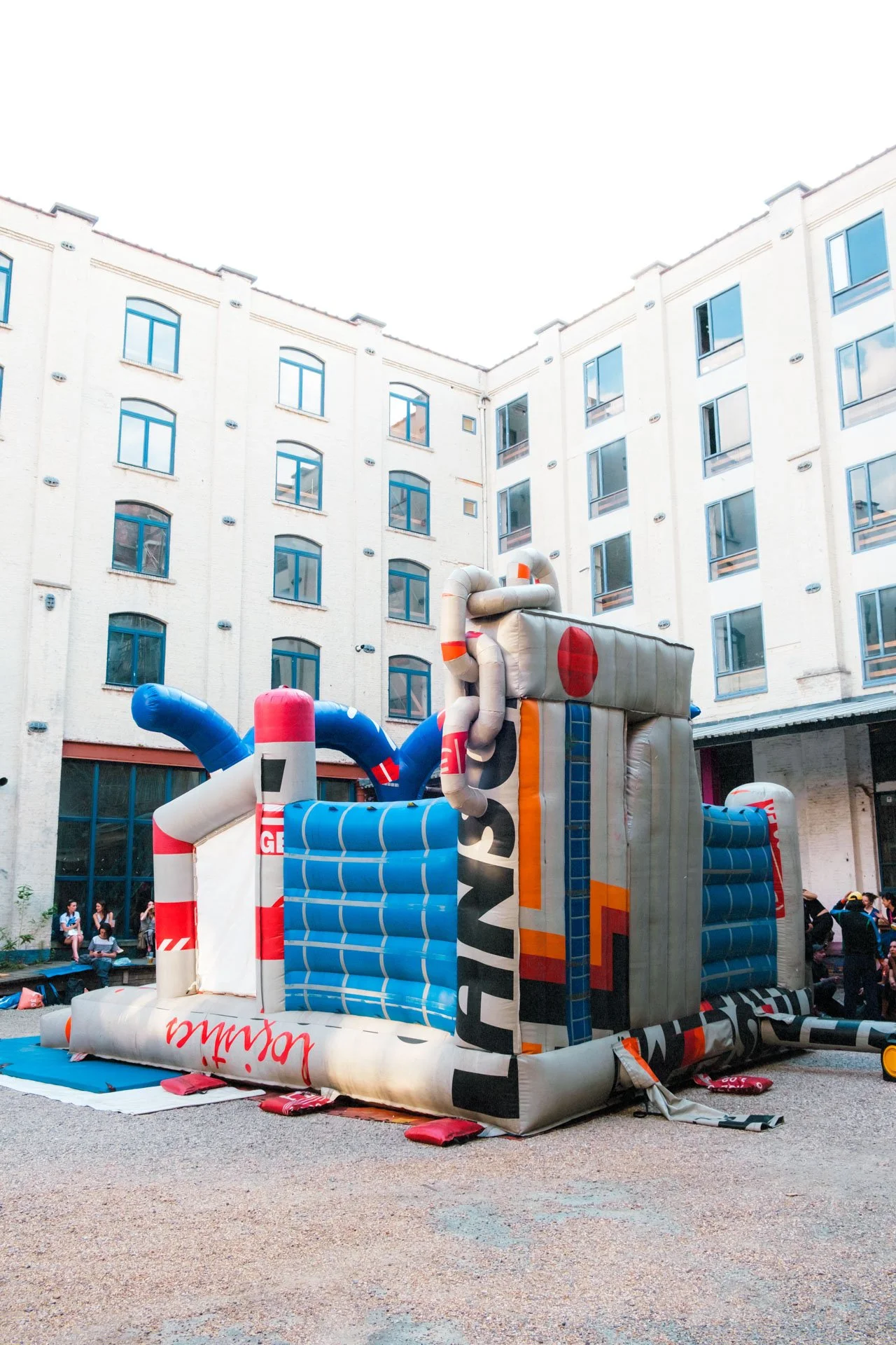 Structure gonflable pour enfants dans une cour entourée d'immeubles résidentiels, avec des personnes assises et se tenant à proximité.