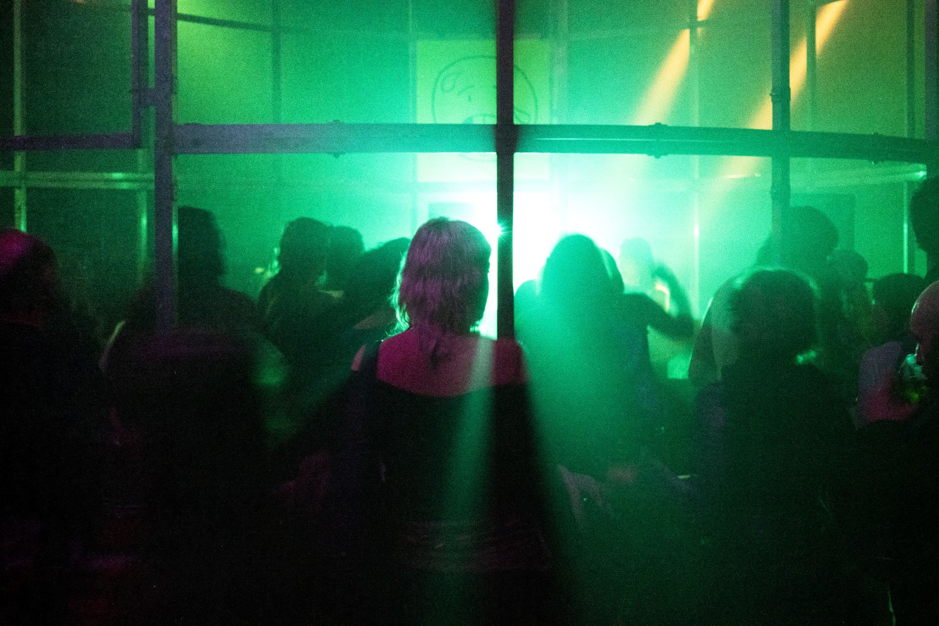 Groupe de personnes dans un environnement sombre avec des lumières vertes et jaunes, probablement dans une discothèque ou un club