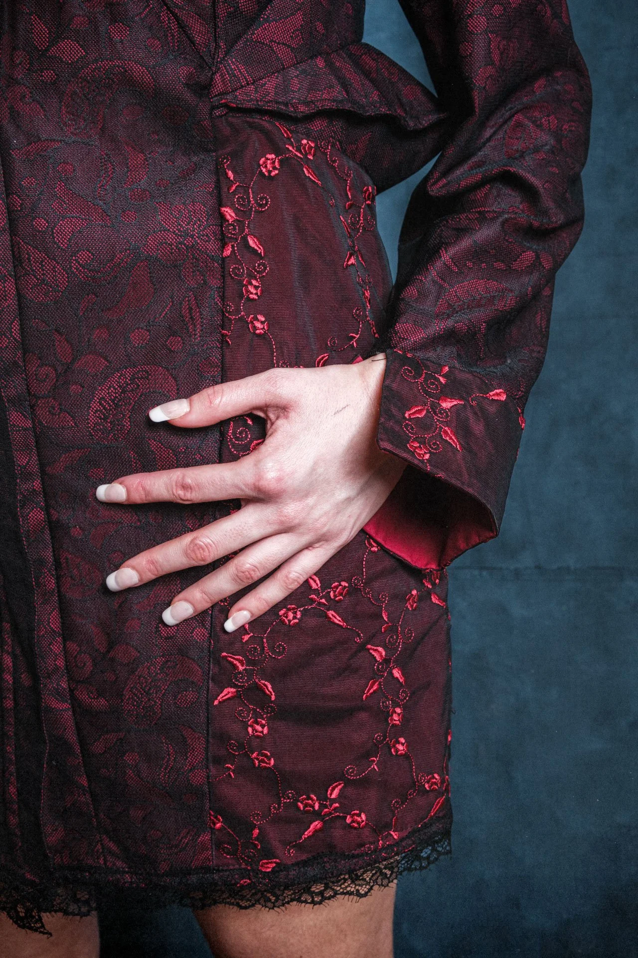 Près d'une personne portant une robe en dentelle rouge avec des broderies florales rouges, la main placée sur la hanche