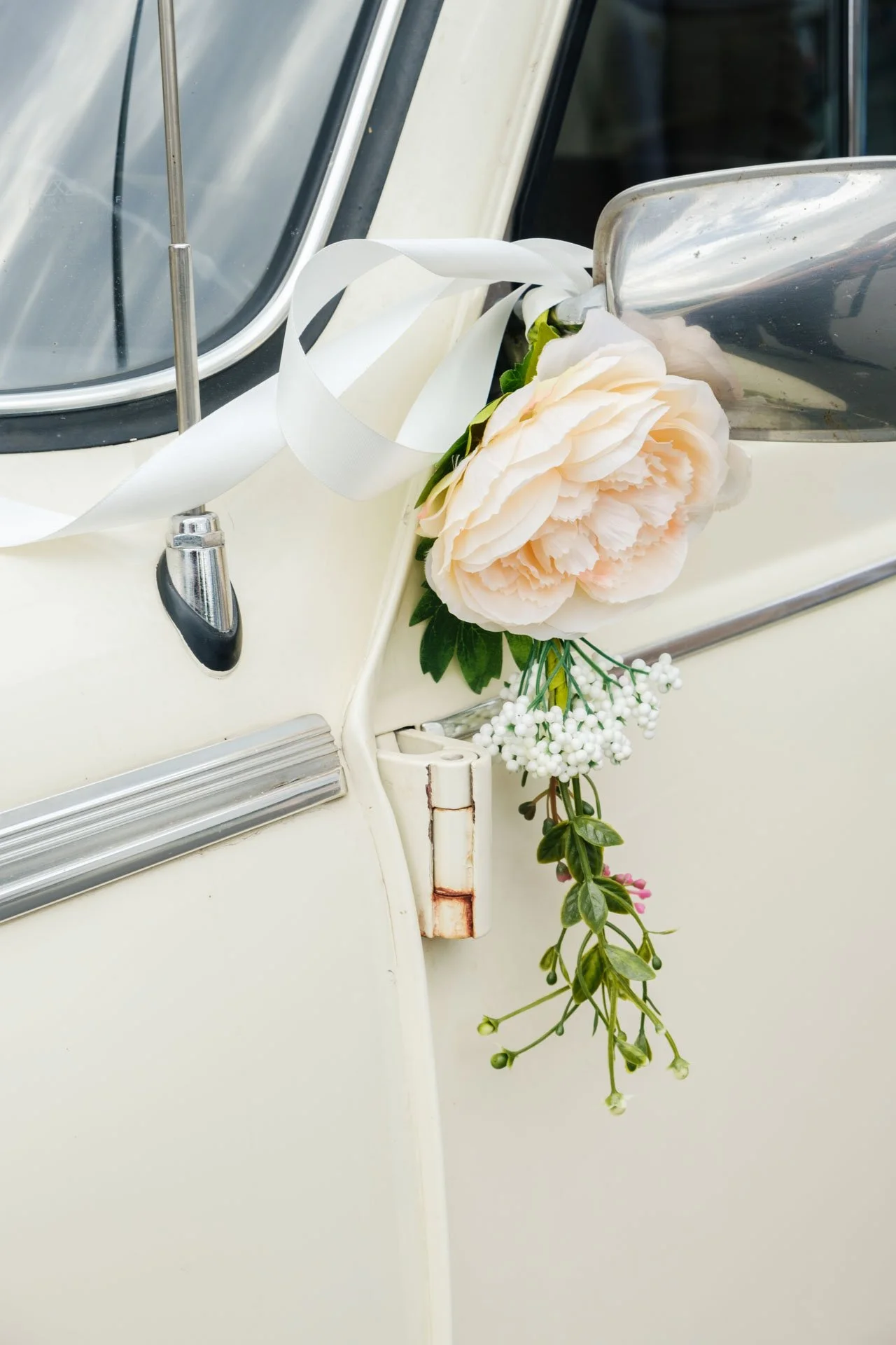 Fleurs blanches et vertes attachées à une voiture vintage blanche.