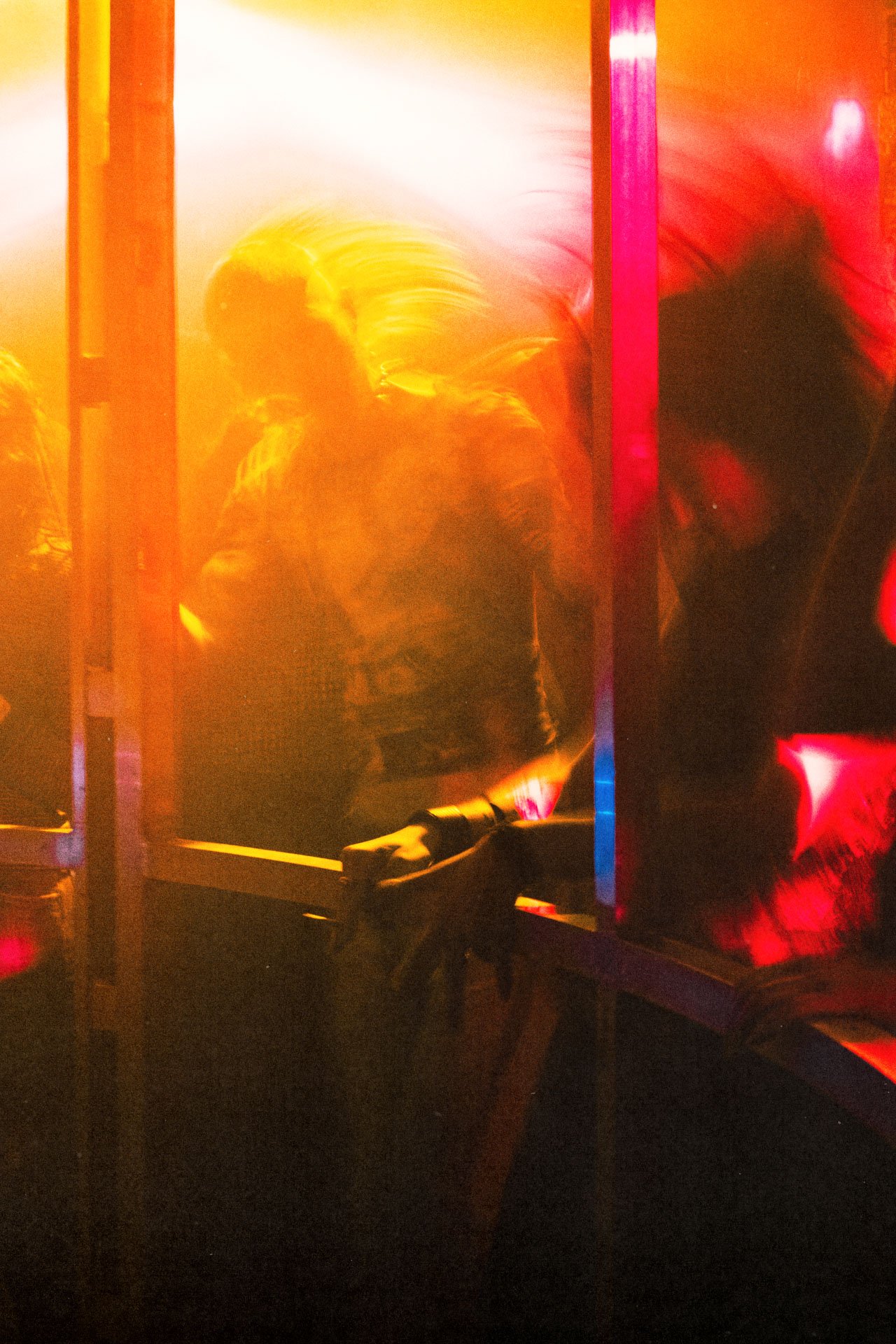 Image floue et colorée avec des reflets de lumières rouges, jaunes et roses. La scène semble être une cabine ou un espace confiné avec des personnes ou des silhouettes à l'intérieur, probablement en mouvement.