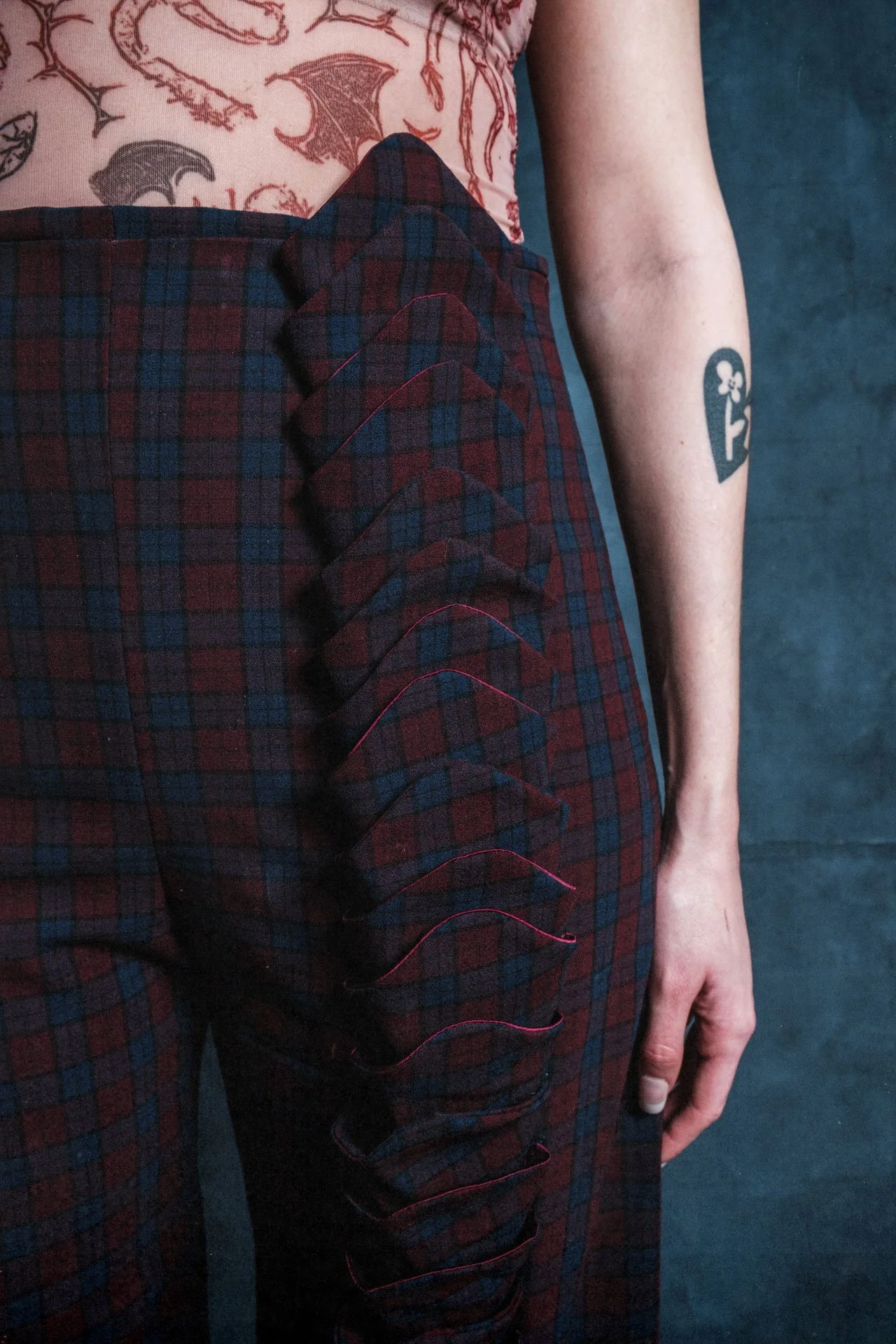Bras droit d'une personne avec un tatouage de clé en forme de trèfle. Vêtements à carreaux rouges et noirs, pantalon à carreaux aux couleurs similaires.